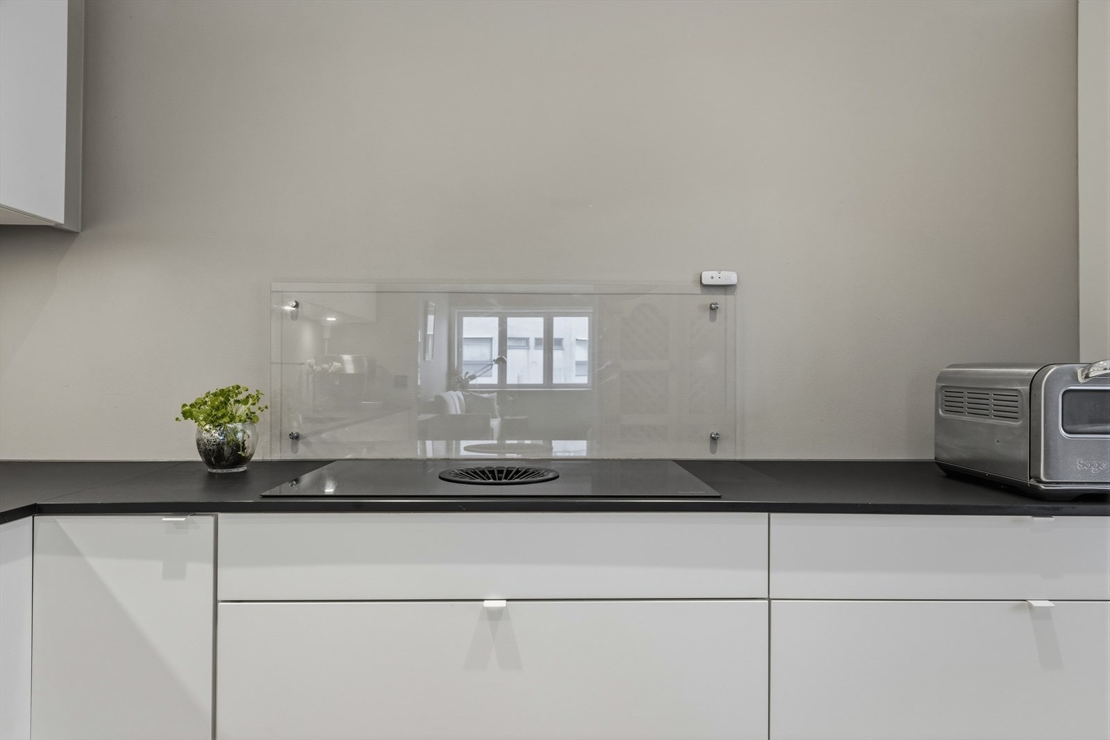 Backsplash i glass bak koketoppen. Benkeplate i kompaktlaminat i matt sort, nedfelt kum og integrert koketopp med kullfiltervifte. Galleribilde