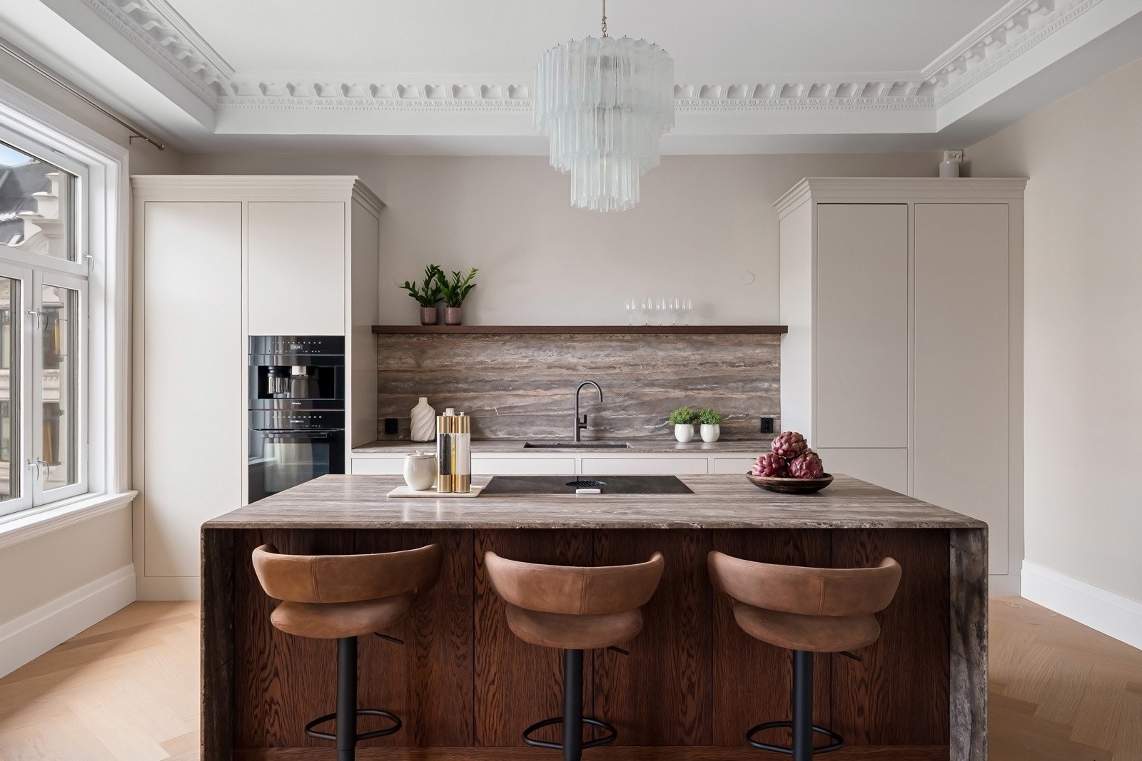 Kjøkkenøya har benkeplate med "waterfall"-utførelse, og benkeplaten videreføres opp som backsplash langs veggen for et helhetlig og eksklusivt uttrykk. Galleribilde