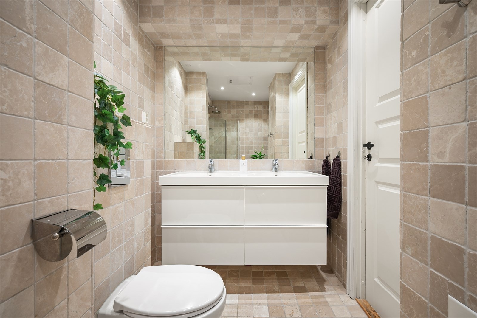 Badet er utstyrt med veggmontert toalett, to servanter med tilhørende innredning, speil, samt dusjhjørne med glassdører og regnfallsdusj - Det er opplegg for vaskemaskin Galleribilde