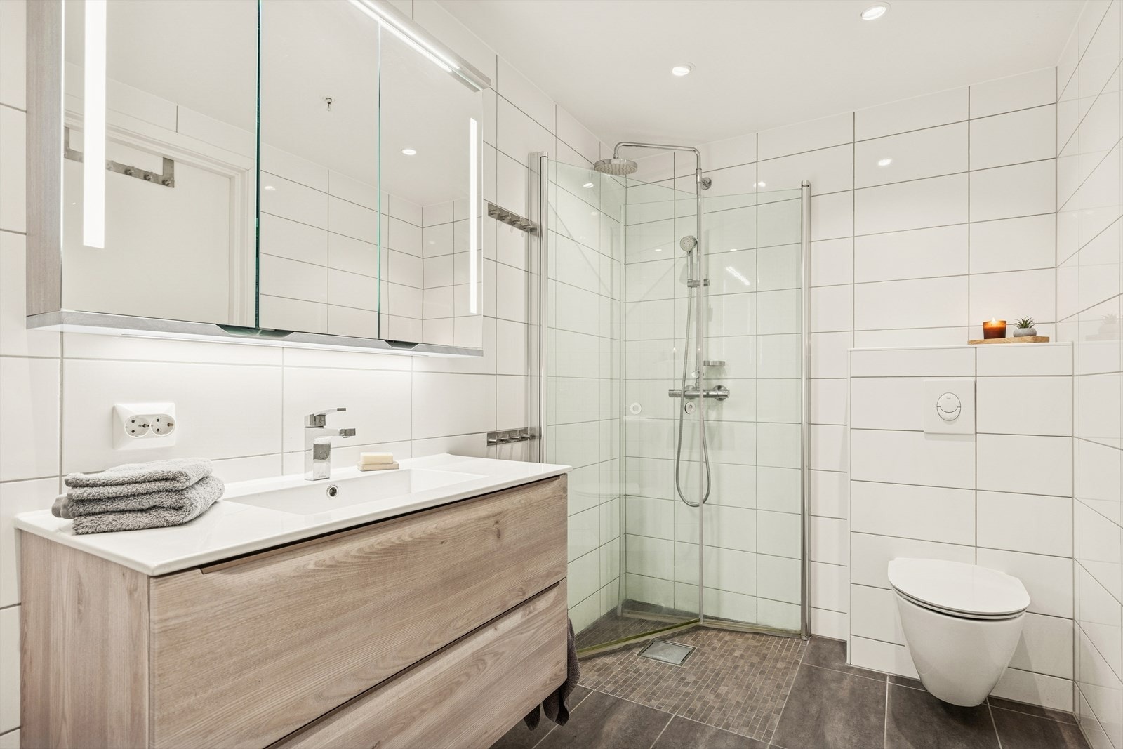 Det er montert dusjdører i glass, og badet har et pent og romslig baderomsmøblement, speil og vegghengt WC. Galleribilde