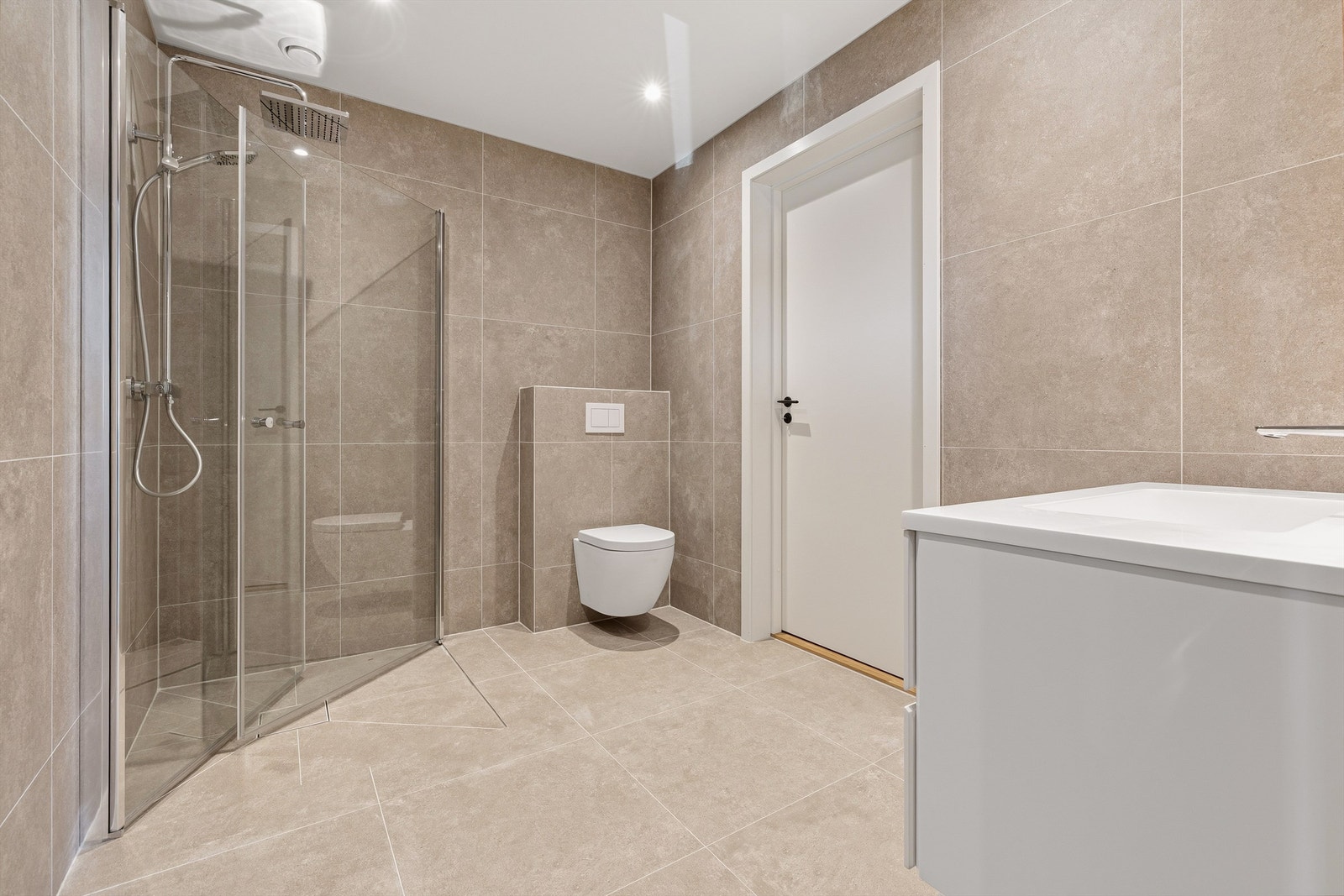 Badene er utstyrt med vegghengt toalett, servant og innfelte glassdører til dusj. Bad første etasje Galleribilde