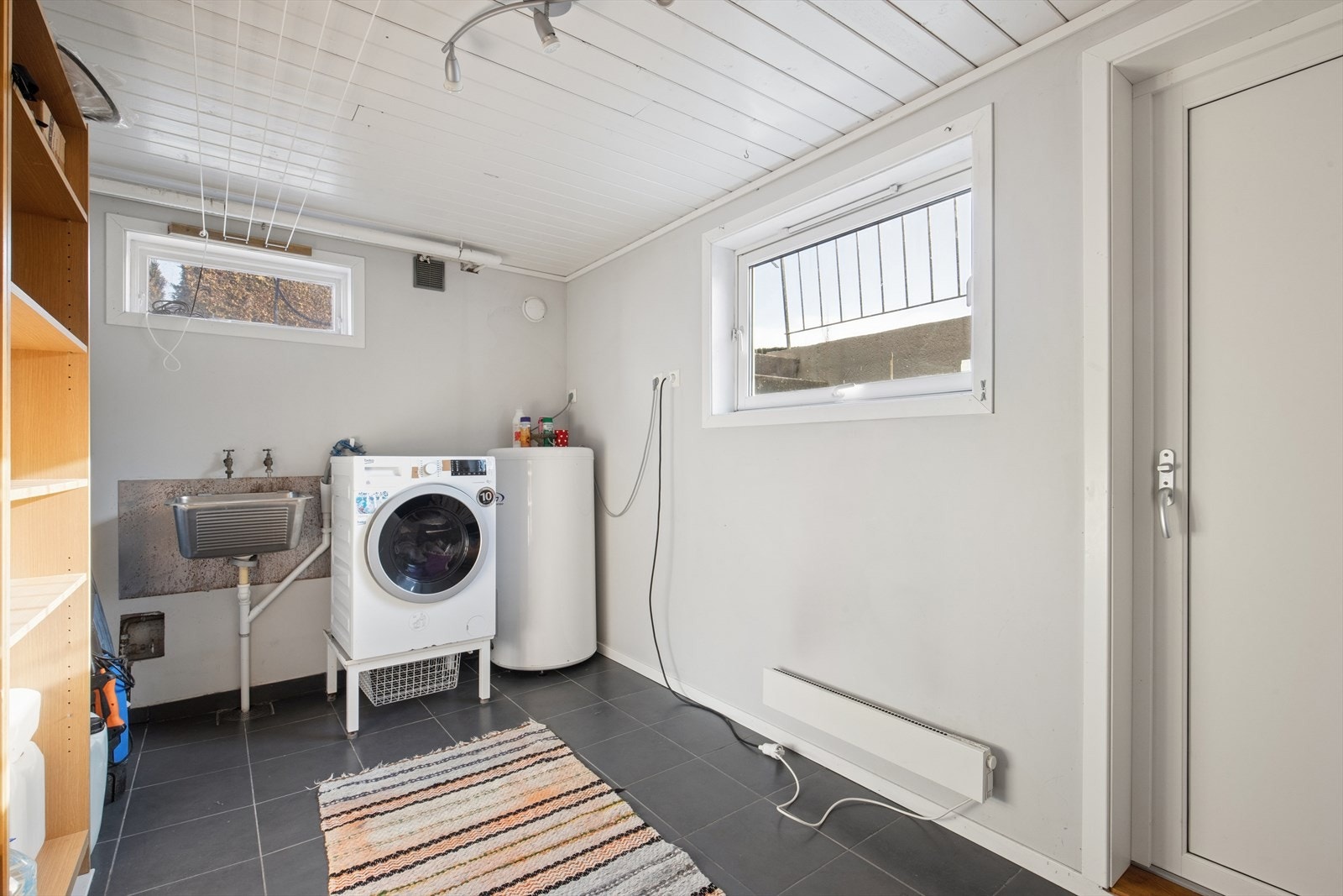 Vaskerommet er romslig og innredet med grå fliser på gulvet og malte veggflater. Rommet er ellers utstyrt med utslagsvask, varmtvannsbereder og opplegg for vaskemaskin. Galleribilde