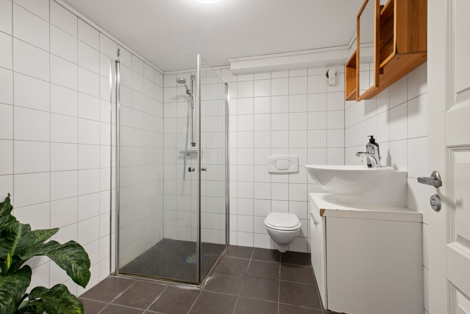 I kjelleren finner man også et baderom hvor grunnbasen er fra byggeår, men er modernisert med flis på flis i nyere tid. Også dette badet er innredet med grå fliser på gulvet og hvite fliser på vegg. Også her har man varmekabler i gulvet. Galleribilde