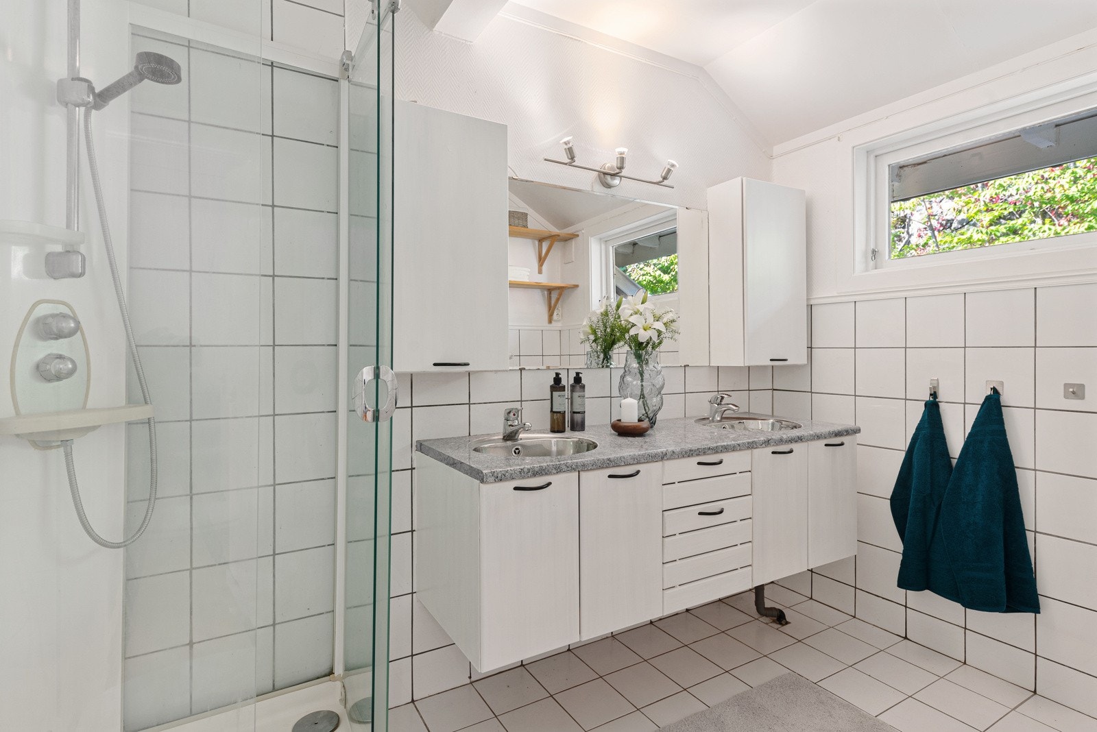 Badet har en hvit innredning med dobbeltservant, et toalett og et dusjkabinett. Galleribilde