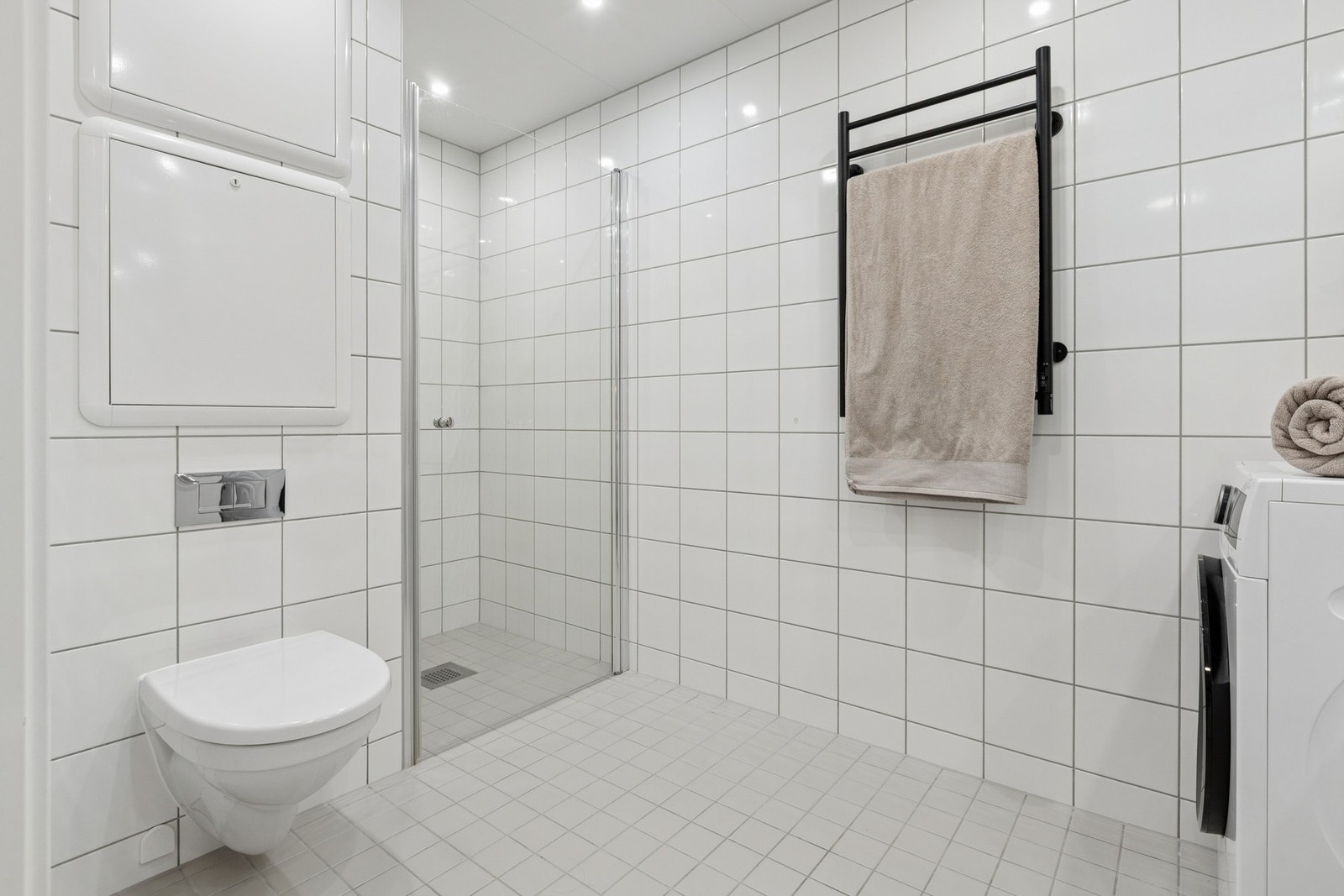 Praktisk og flislagt bad utstyrt med servantinnredning med oppbevaring, speil og opplegg for vaskemaskin. Galleribilde