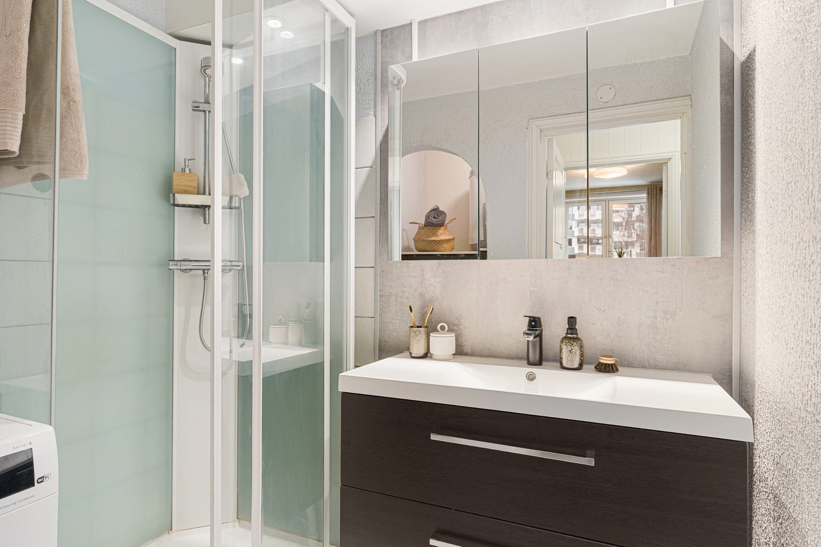 Badet er innredet med dusjkabinett og servantskap. Videre er det speilskap og lys over servant samt opplegg for vaskemaskin Galleribilde