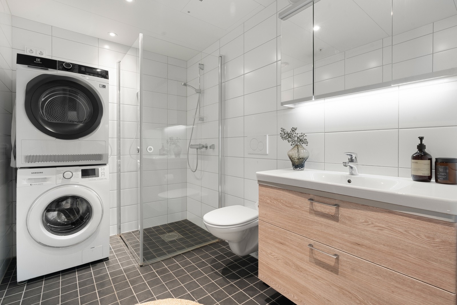 Delikat bad med praktiske løsninger som vegghengt toalett, hjørnedusj og plass til vaskemaskin og tørketrommel.