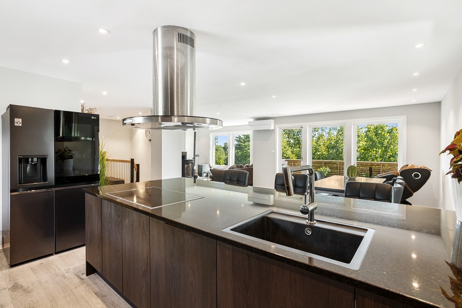 Stor kjøkkenøy med fritthengende ventilator i åpen løsning mot det grønne. Galleribilde