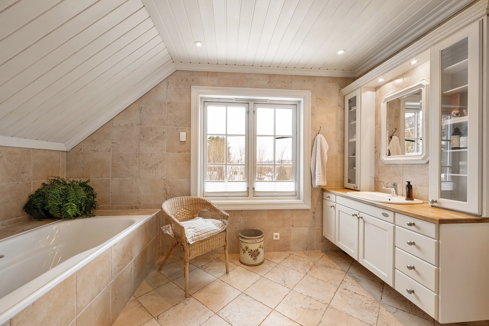 Badet er innredet med nedfelt servant med servantskap, overskap med veggmontert speil, vegghengt toalett samt flislagt badekar og dusjvegger i glassbygestein Galleribilde