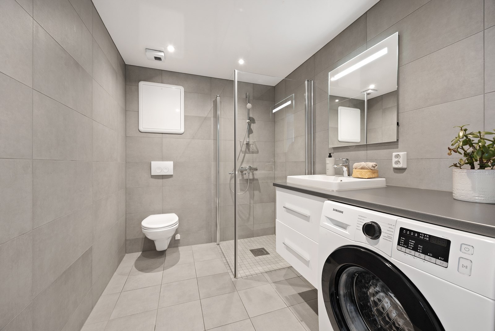 Moderne, flislagt bad fra 2023 med veggfestet klosett og dusj på gulv. Galleribilde