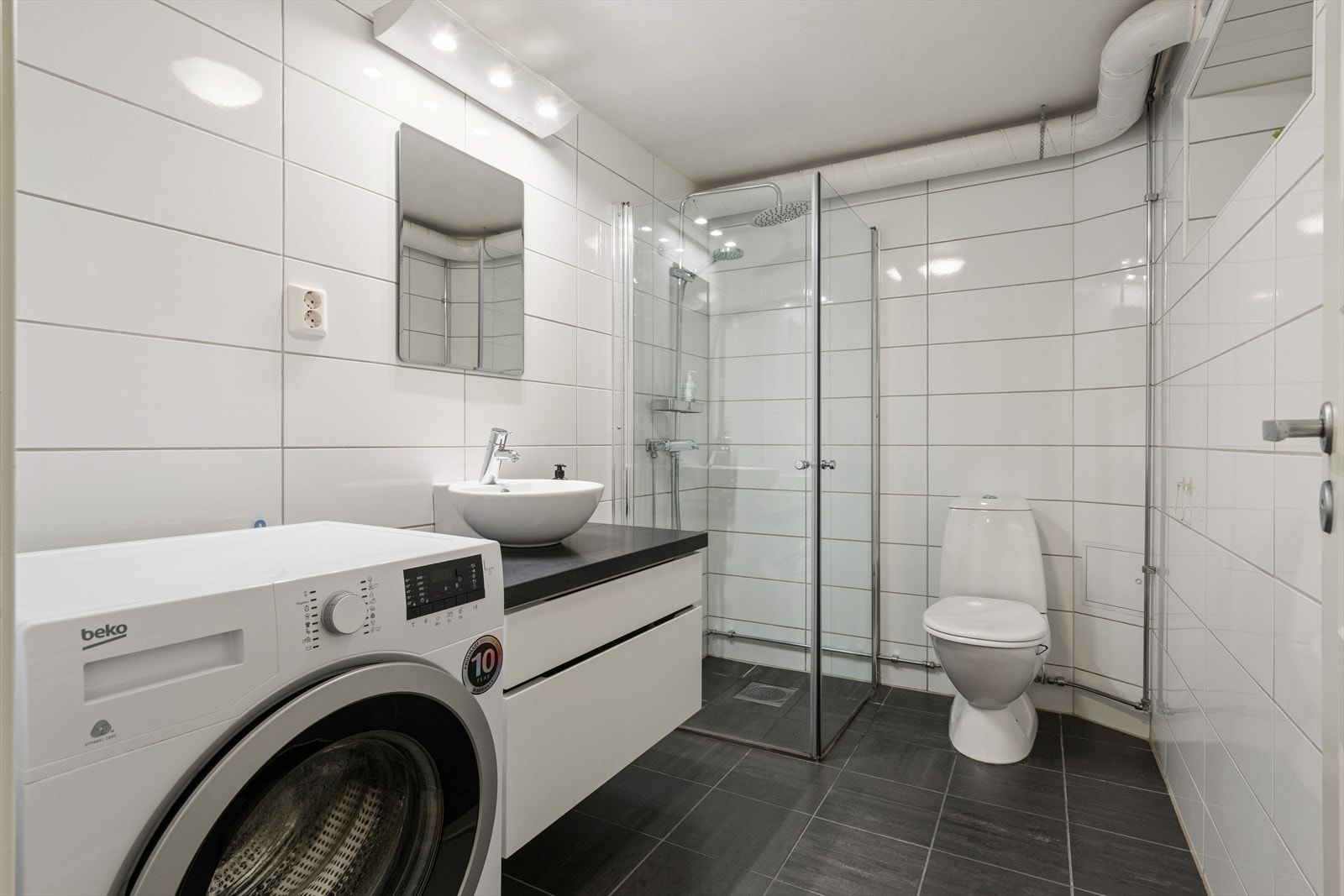 Badet er helfliset og har dusjhjørne, servantinnredning og opplegg for vaskemaskin. Galleribilde