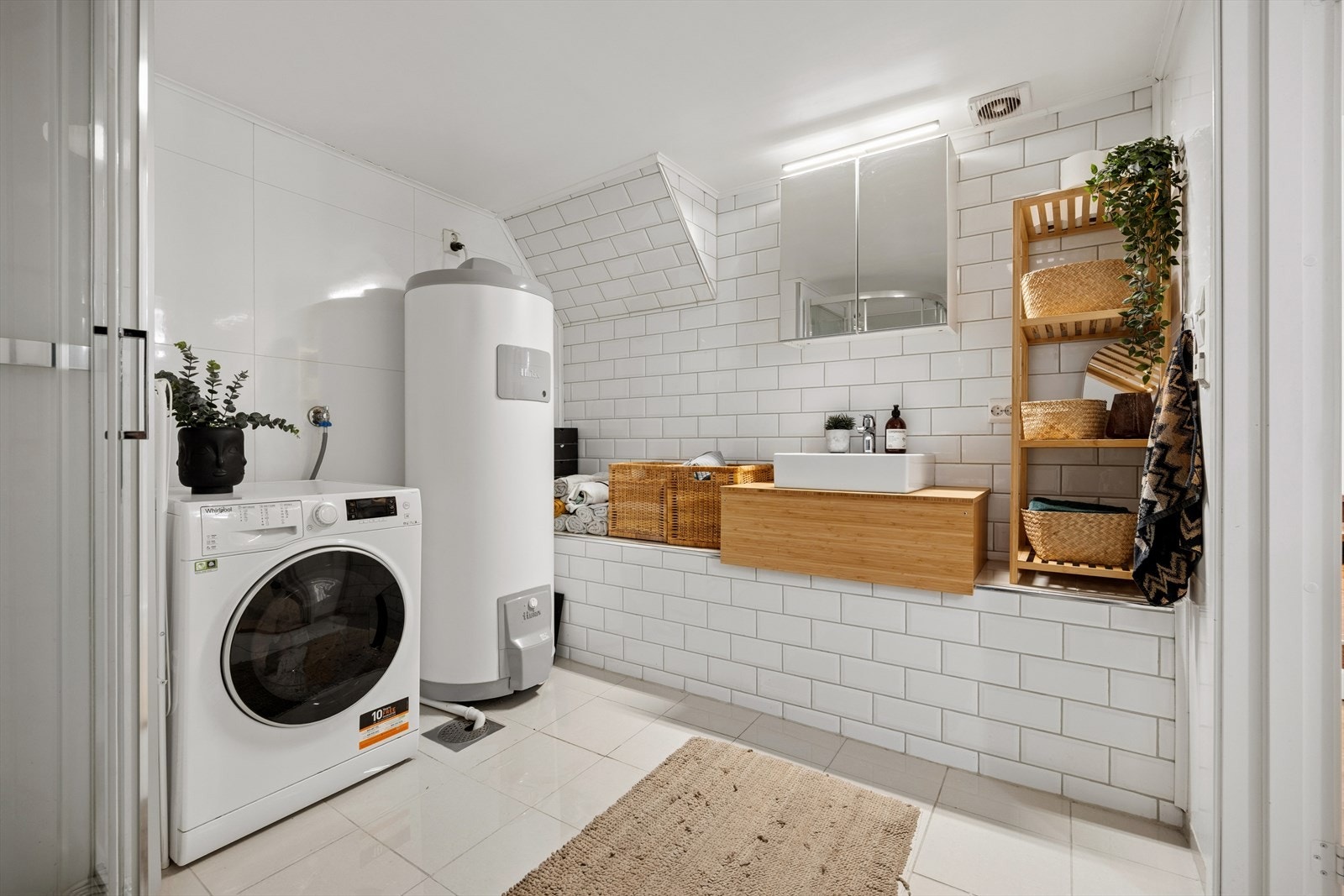 Et moderne bad fra 2019 med flislagt gulv med varme i gulv og våtromsplater/flis på veggene. Innredningen består av servantinnredning, dusjkabinett, veggmontert toalett og opplegg for vaskemaskin. Galleribilde