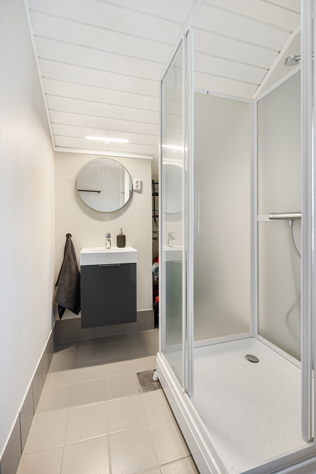 Badet har lysmalte vegger og gråmalte fliser på gulv med gulvvarme. Galleribilde