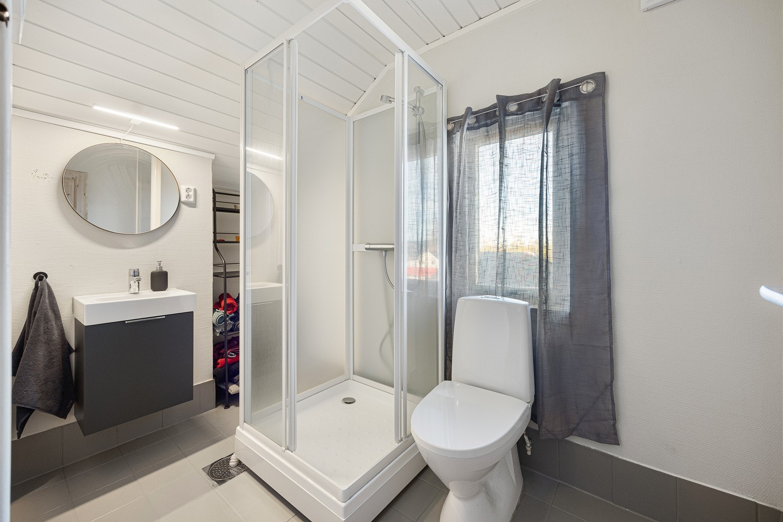 Baderomsinnredningen består av en grå servantseksjon og speil med belysning, og badet har videre et toalett og et nyere dusjkabinett. All innredning på badet er fra 2025, og det ble i 2026 installert ny avtrekksvifte. Galleribilde