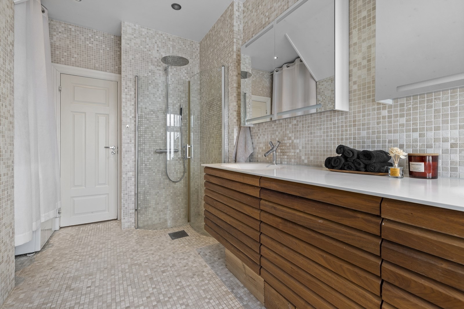 Her er det flislagt gulv og flislagte vegger som gir et tidløst og helhetlig uttrykk. Innredningen består av benkeskap med profilerte fronter og veggskap med speilfronter, noe som gir både god oppbevaring og et elegant preg. Galleribilde