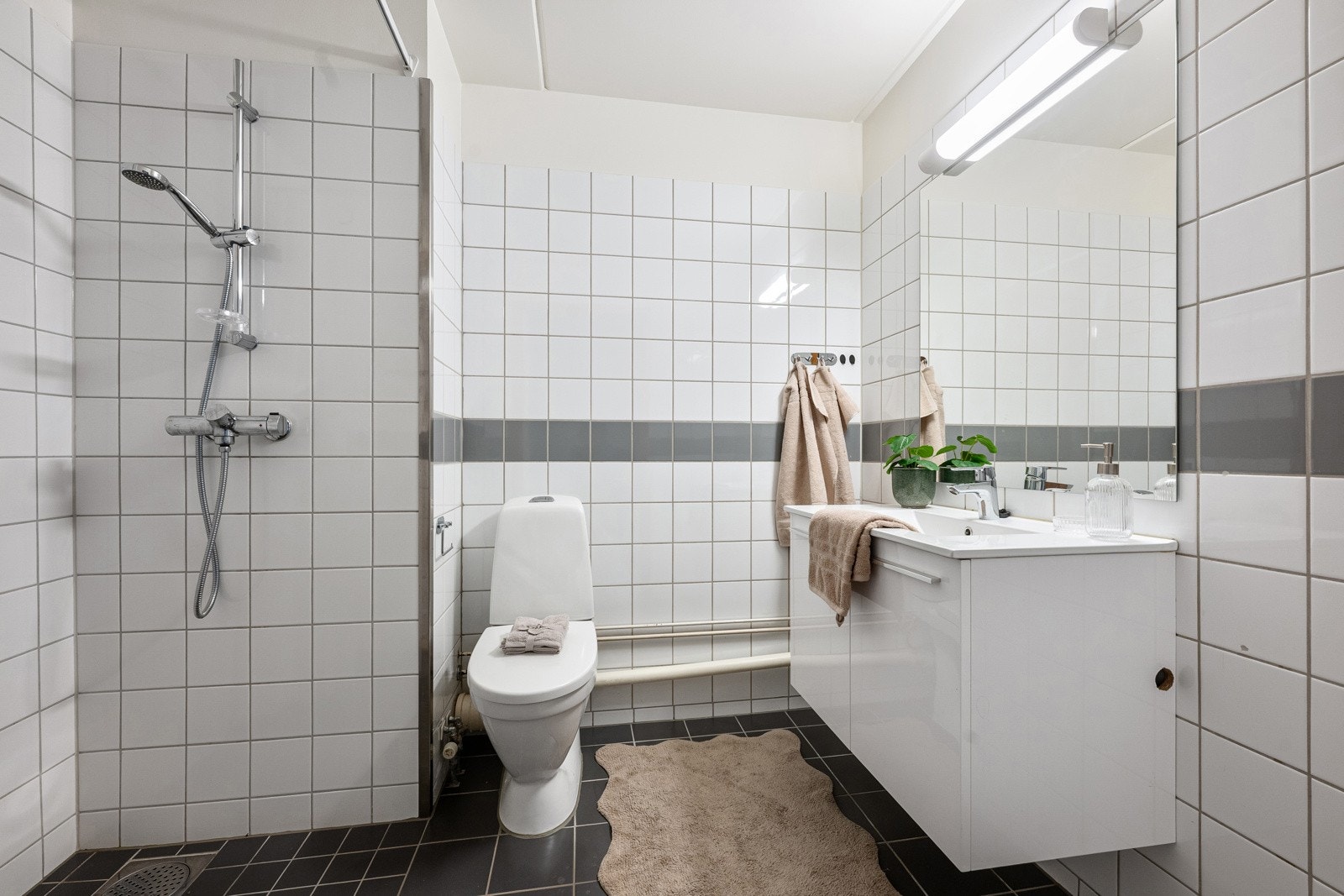 Romslig flislagt bad innredet med servant, speil med lys, toalett og opplegg for vaskemaskin. Galleribilde