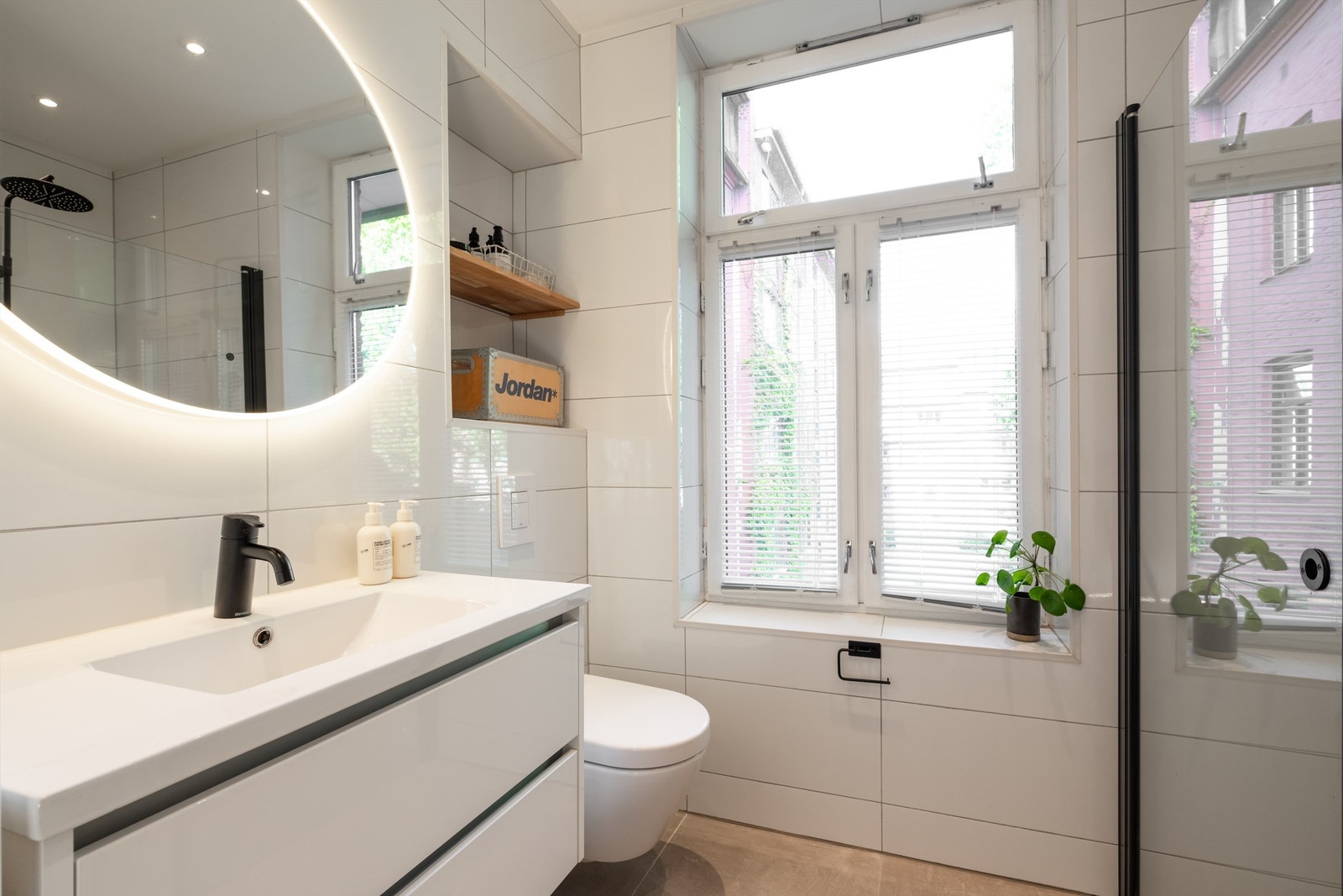 Rommet er innredet med vegghengt toalett, servantinnredning med skuffer og ovenpåliggende vask og stilrent speil med sidelys. Galleribilde