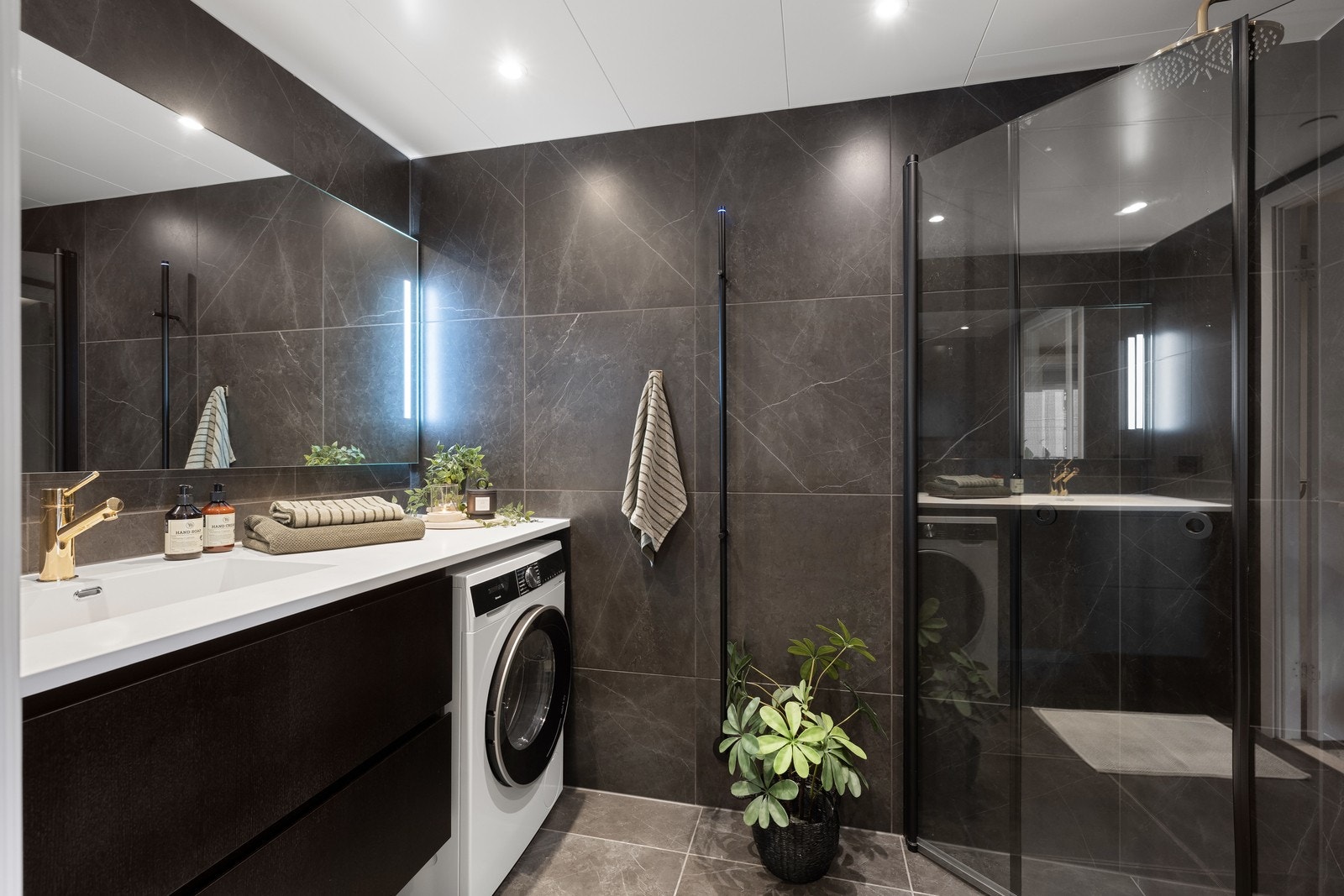 Badet er lekkert med mørke fliser på vegg og gulv. Romslig bad med opplegg til vaskemaskin og flere lekre detaljer. Galleribilde
