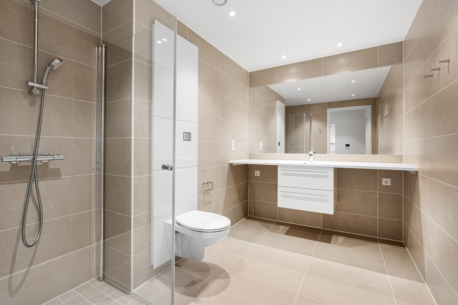 Badet er helfliset med varme i gulvet og inneholder en dusjnisje med innfellbare dusjdører, vegghengt toalett, samt baderomsinnredning med benk slik at du kan ha vaskemaskin og tørketrommel under. Galleribilde