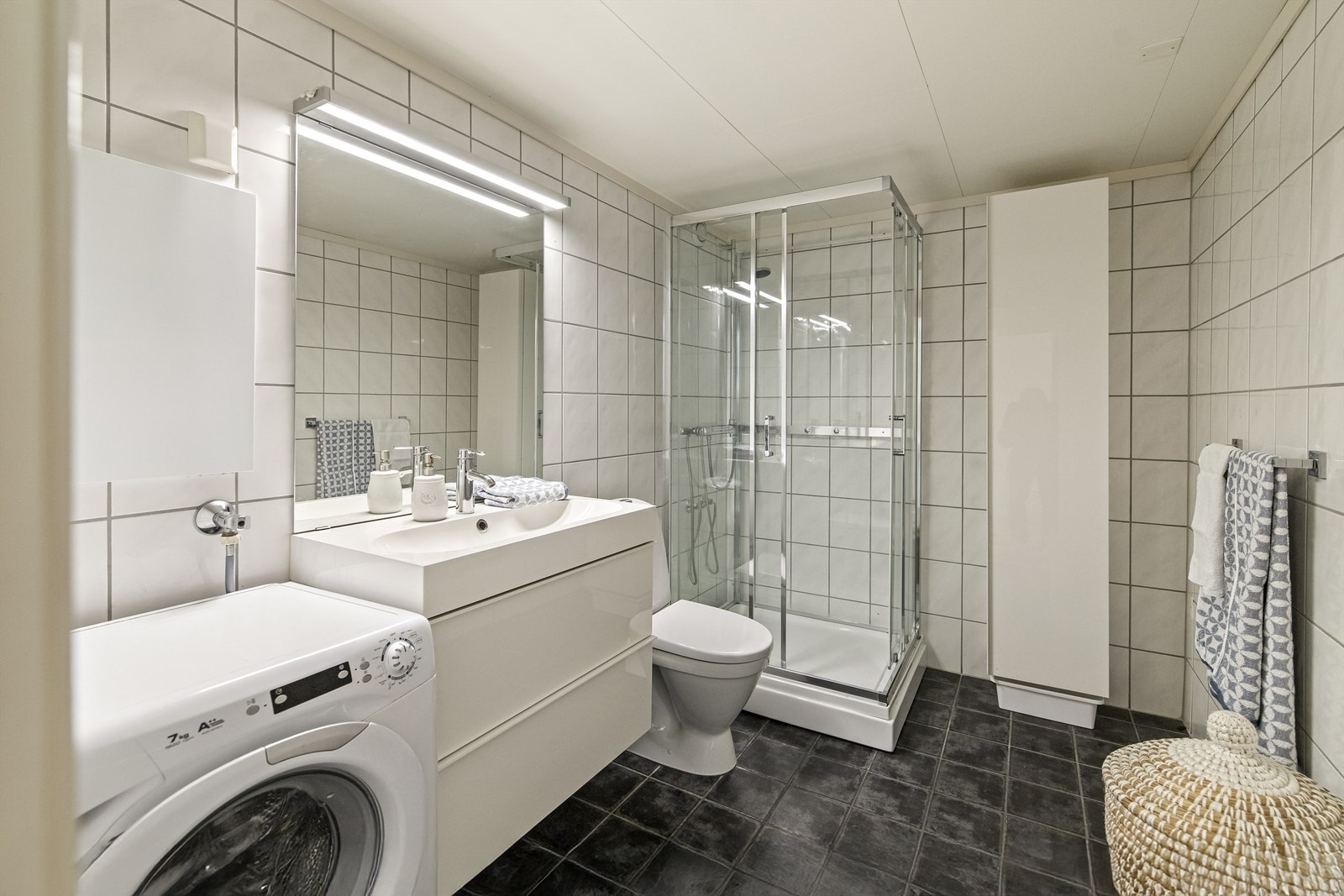 Pent flislagt bad fra ca. 2010 med varmekabler i gulvet. Det er montert innredning med slette fronter, heldekkende servant og ett greps armatur. Speil, overlys og stikkontakt. Dusjkabinett og gulvstående toalett. Badet har også opplegg til vaskemaskin. Galleribilde