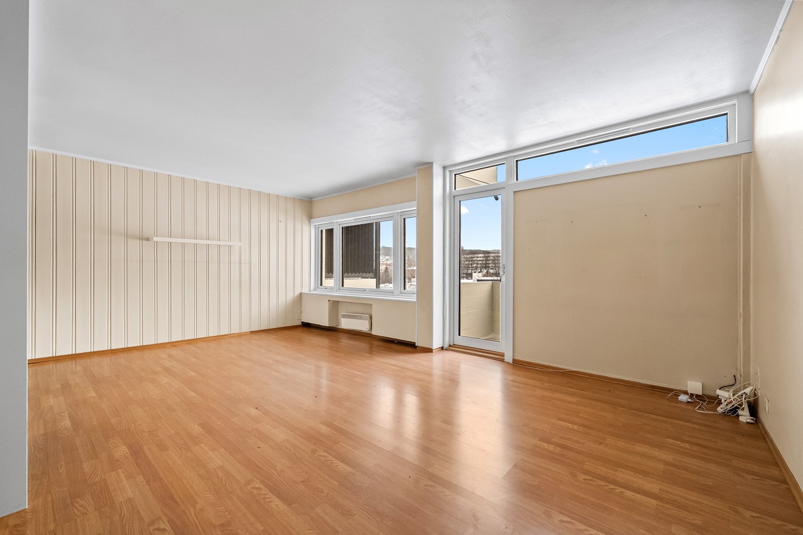 Stue med lysmalte veggflater og laminat på gulv. Store vindusflater slipper inn godt med dagslys og bidrar til en luftig romfølelse. Galleribilde