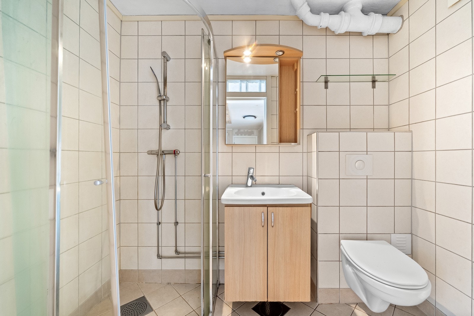 Flislagt bad av eldre dato (eksakt alder er ikke kjent). Badet er innredet med servantmøblement, speilskap, vegghengt toalett og separat dusjhjørne. Galleribilde