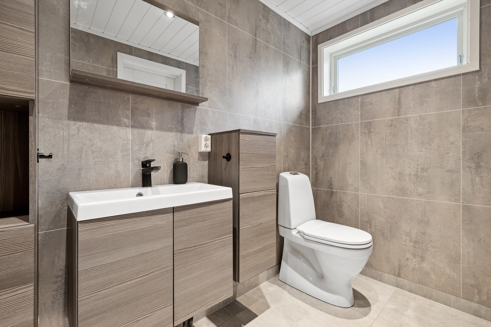 Badet er utstyrt med toalett, åpen dusj, stor baderomsinnredning med servant og opplegg for vaskemaskin. Galleribilde