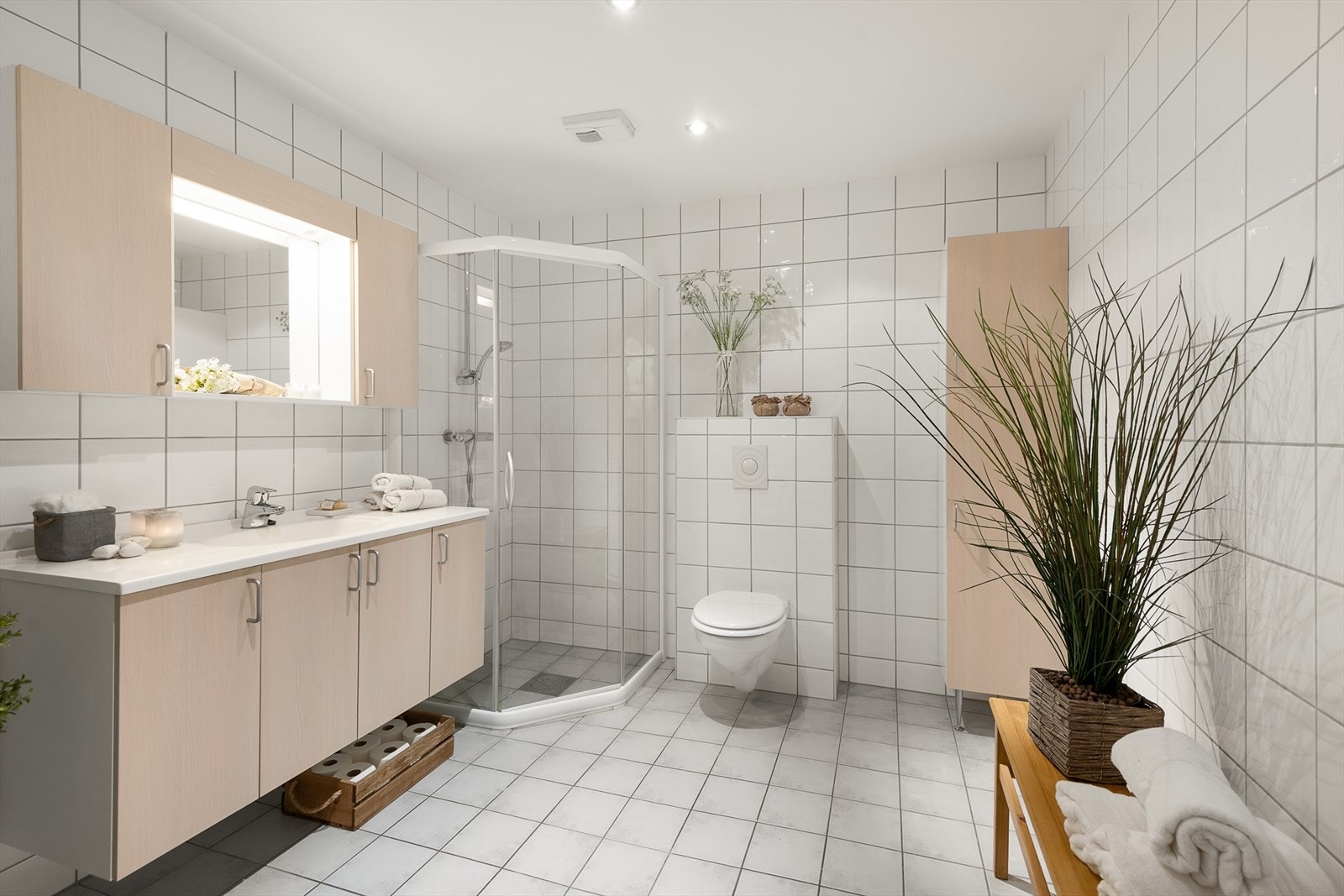 Pent og romslig bad/wc med fliser på gulv og vegger. Dusjhjørne og vegghengt WC. Spotter i tak. Galleribilde