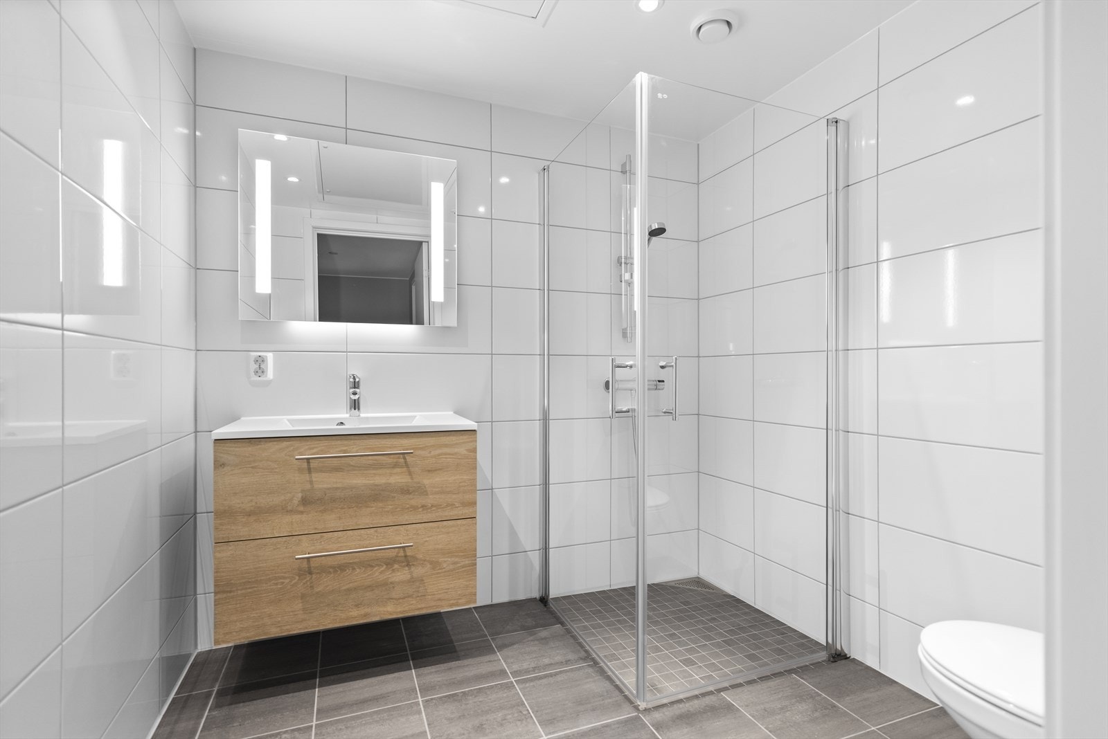 Moderne og stilrent baderom med flislagt gulv med varmekabler og flislagte vegger. Innfelte downlights i himlingen gir god belysning Galleribilde