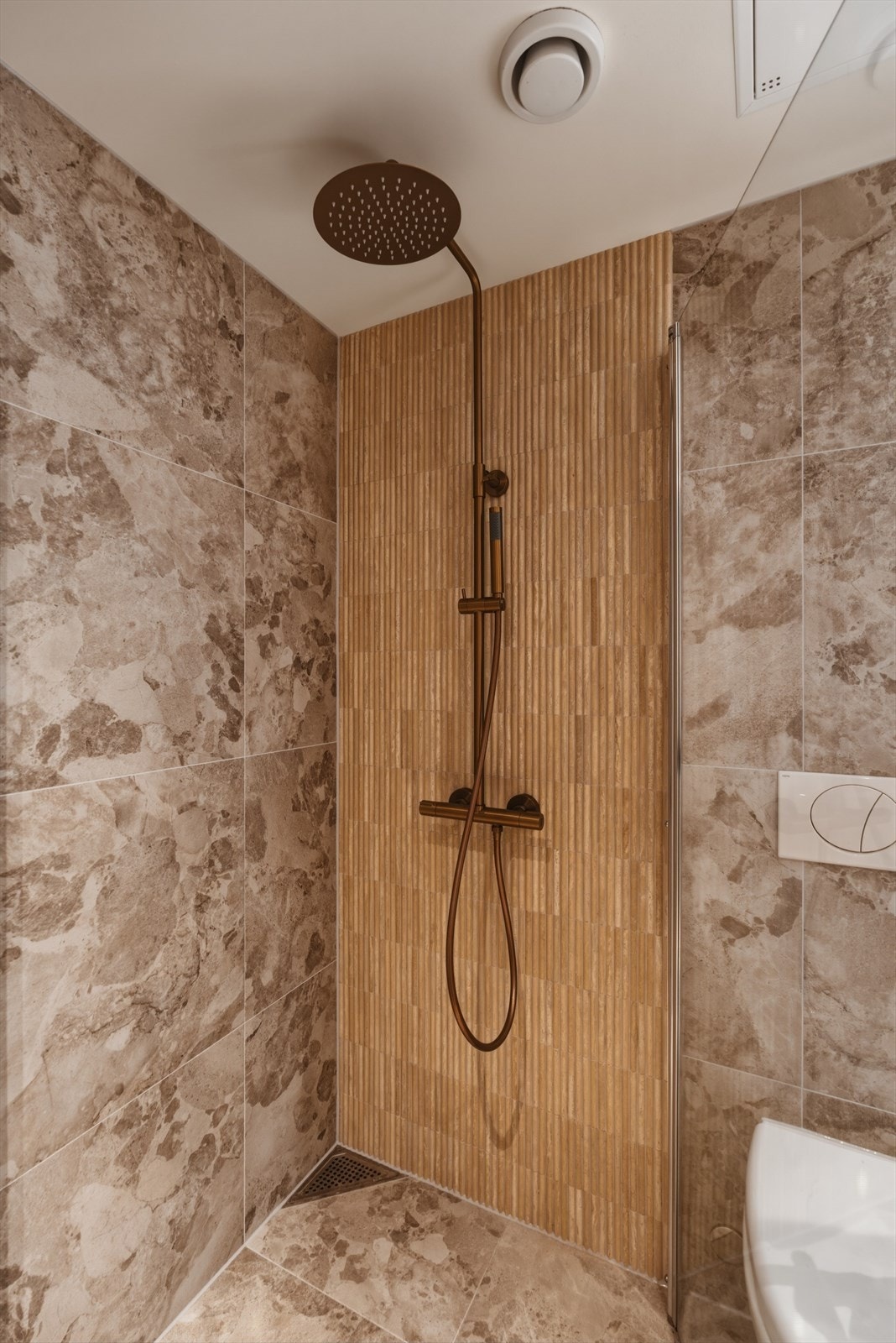 Badet er innredet med vegghengt toalett, dusjhjørne med glassvegger og servantinnredning med skuffer samt speil med integrert belysning. Galleribilde