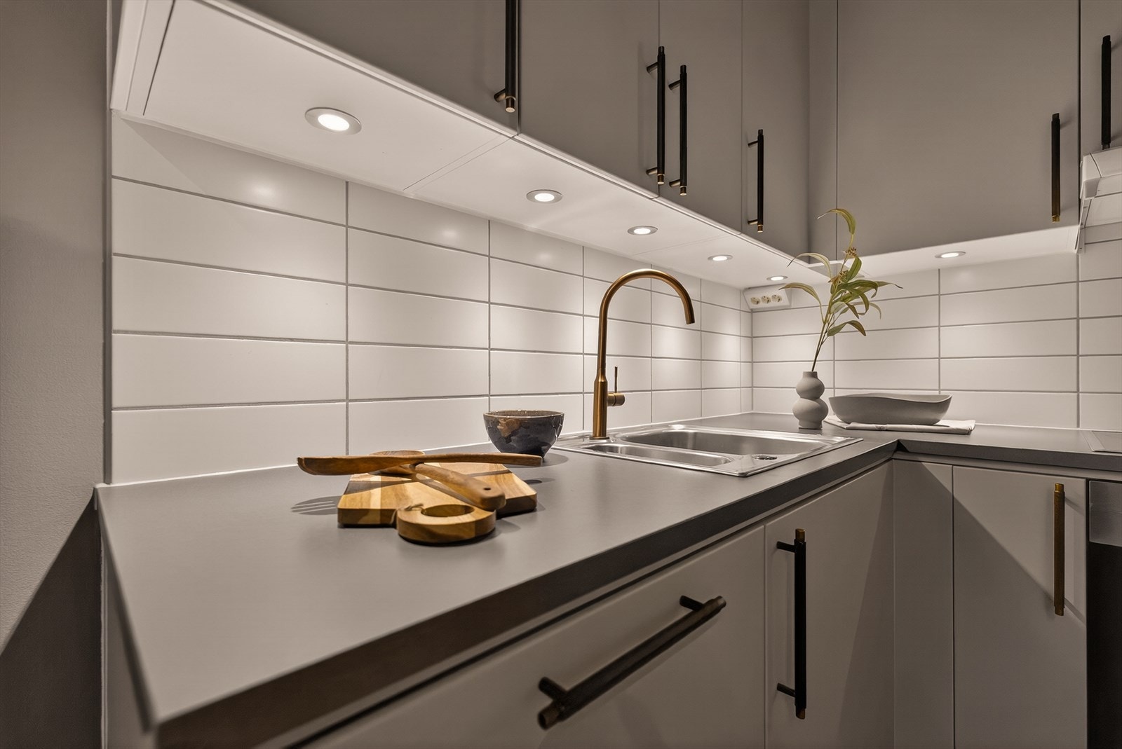 Lys og tidløs kjøkkeninnredning med laminert benkeplate, kjøkkenkran og oppvaskkum, god skap- og benkeplass, samt belysning under overskap. Galleribilde