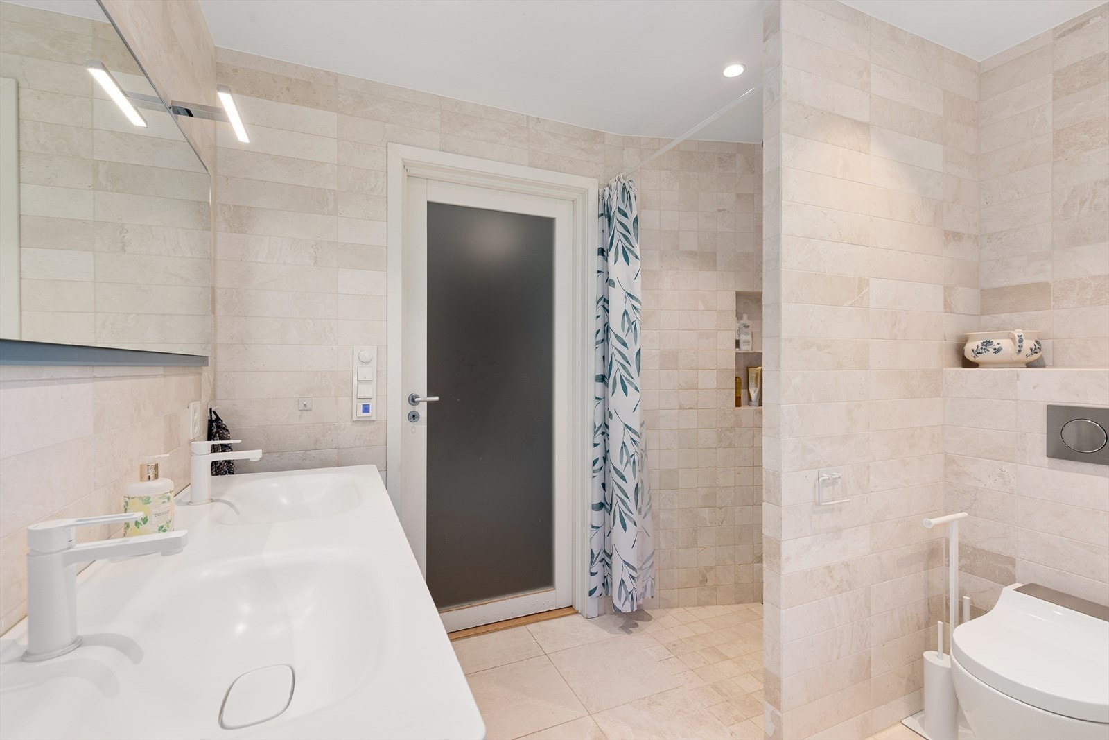 Bad fra 2020 fremstår romslig og delikat, med dobbel servant, speil, Geberit bide toalett og dusjhjørne med innfelte nisjer. Galleribilde