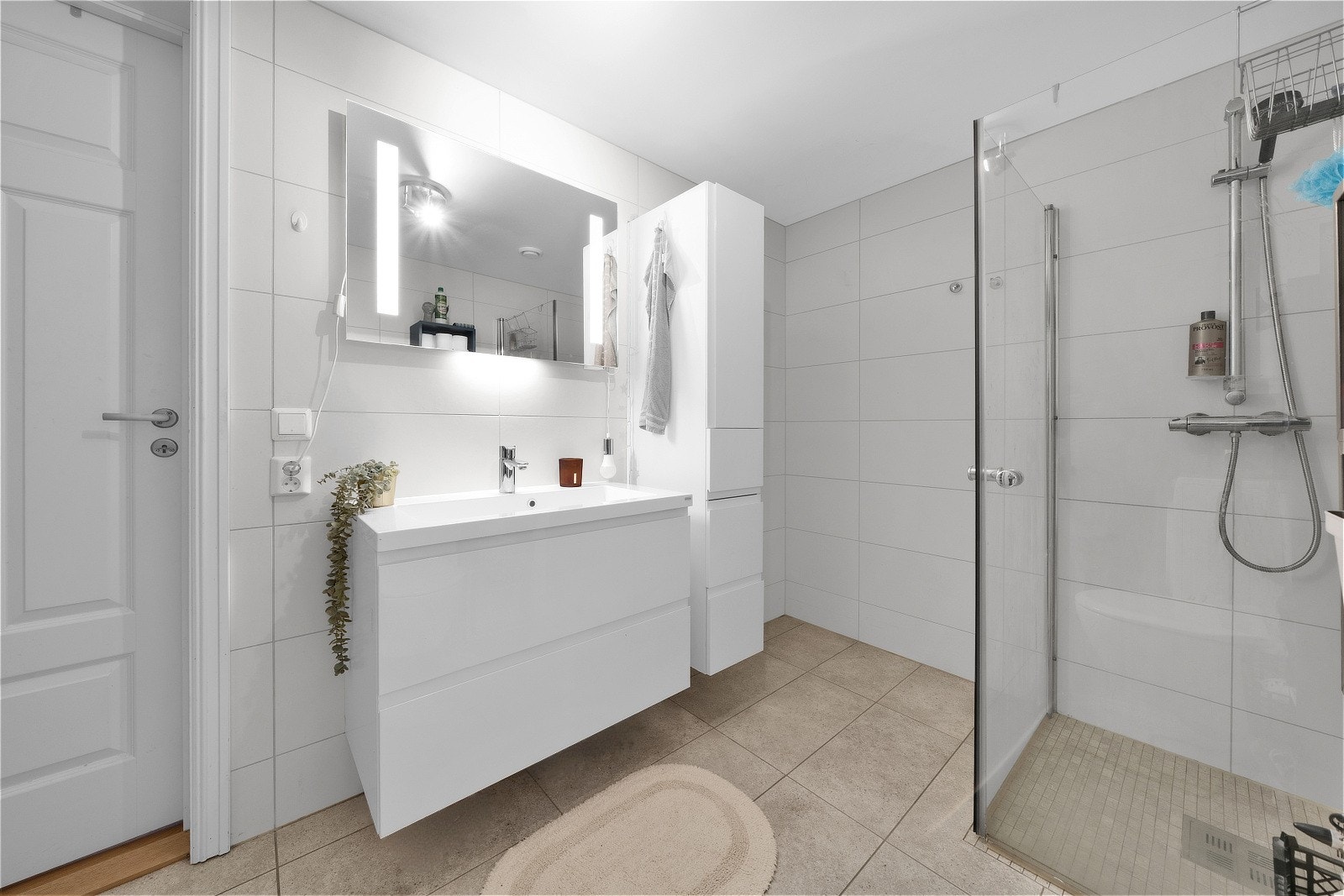 Badet har flislagte vegger, støpt gulv med vannbåren varme, servant med skuffeseksjon, vegghengt toalett, svingbare dusjvegger i glass og opplegg for vaskemaskin. Galleribilde