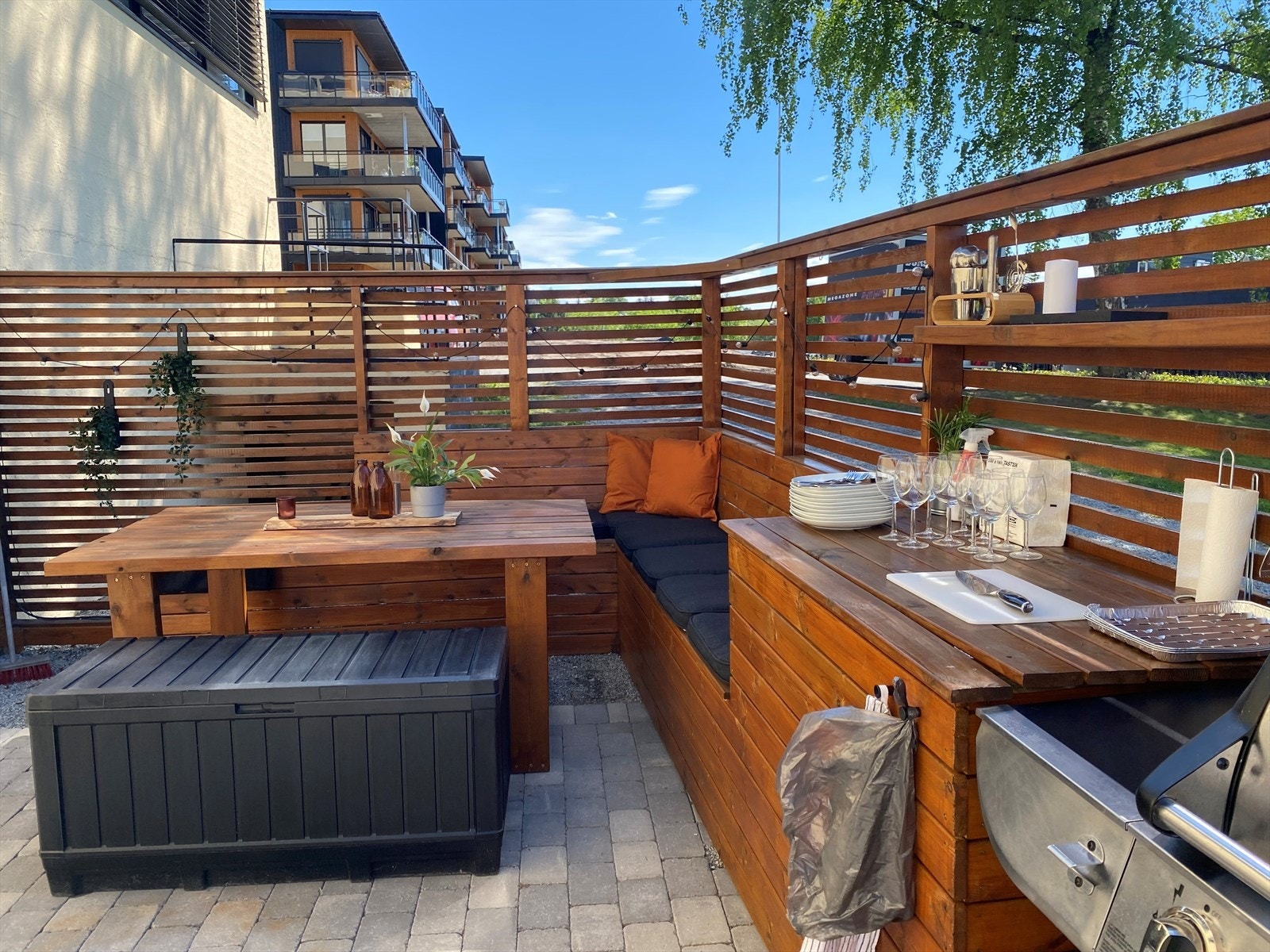 Plassen har brostein på bakken og en praktisk sittebenk, bord, plass for grill og avlastningsbenk. Galleribilde