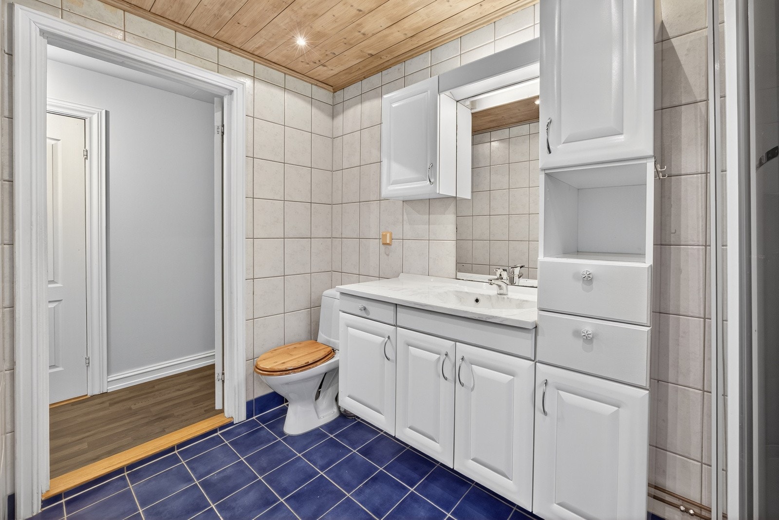 Baderomsinnredningen består av vegghengt servantinnredning med profilerte fronter og tilhørende skap, samt speil over servant. Videre har badet gulvstående toalett og dusjkabinett. Det er montert spottere i taket. Galleribilde