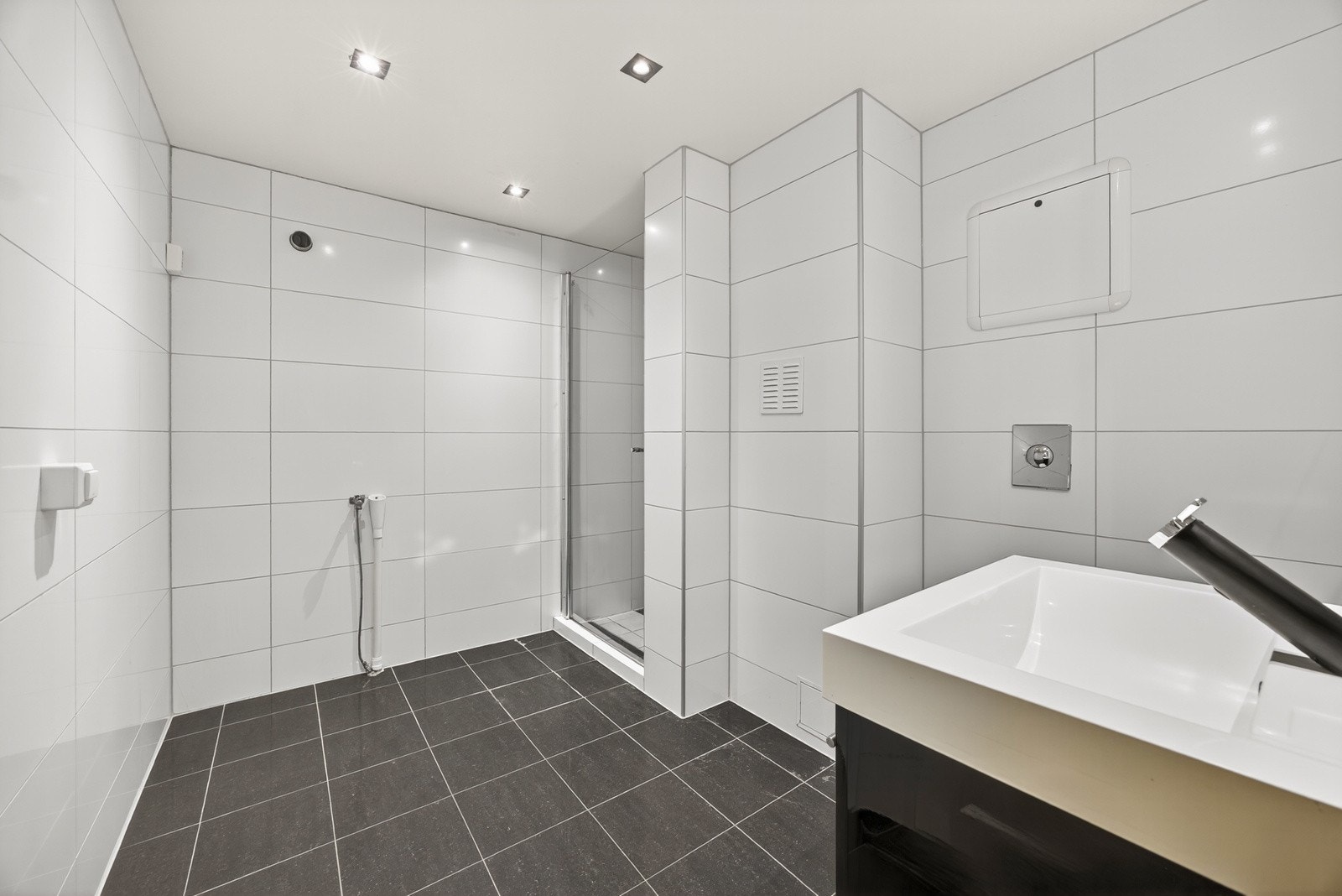 Eldre bad i u.etasjen, fra 2014 iht. tidligere tilstandsrapport. Badet har flislagte overflater og varmekabler i gulv. Baderomsinnredningen består av vegghengt servantmøblement med skuffer, samt speil over servant. Galleribilde