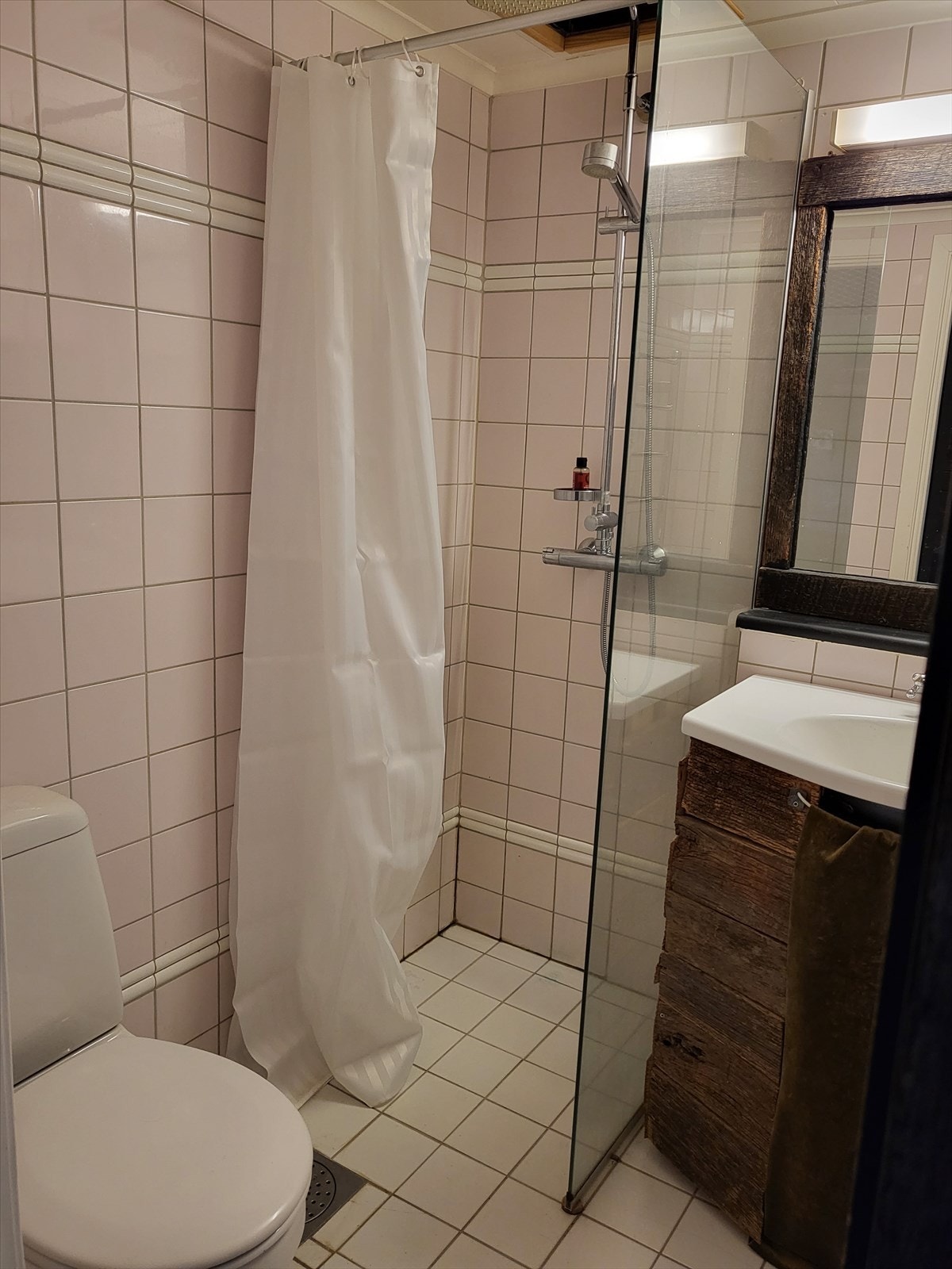 Badet er innredet med åpen dusjløsning, gulvstående toalett og servant med innredning i rustikt treverk som harmonerer med resten av leiligheten. Galleribilde