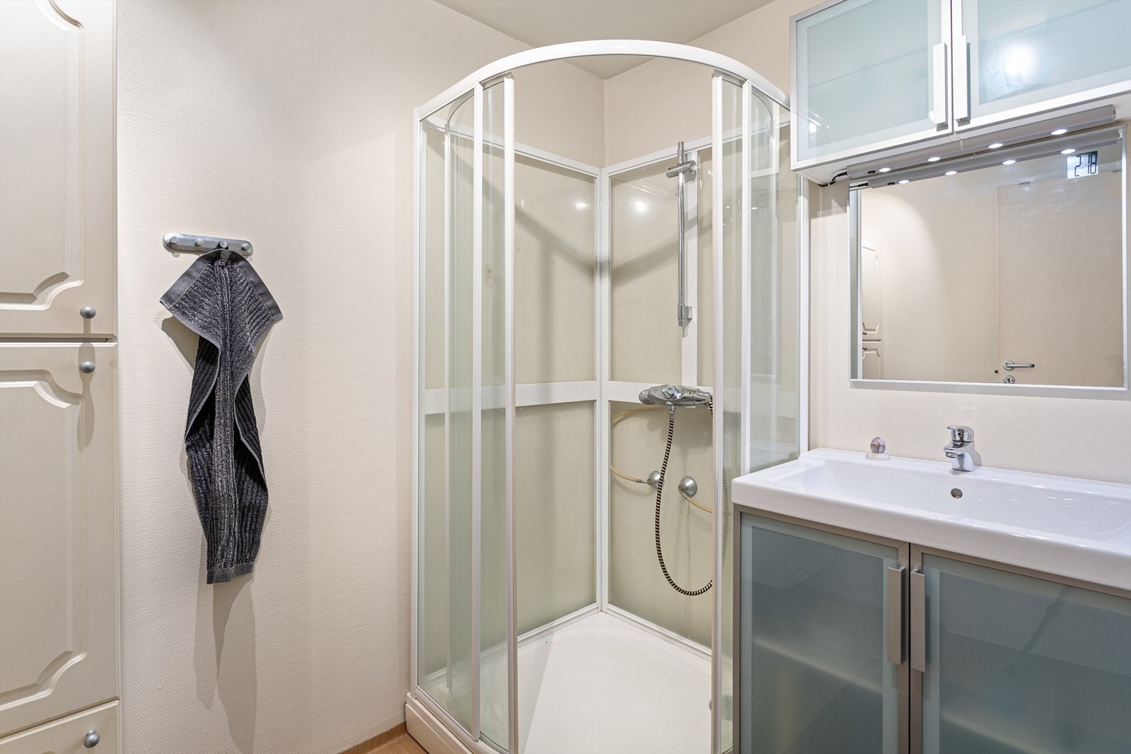 Enkelt bad med dusjkabinett, skap og servant. Galleribilde