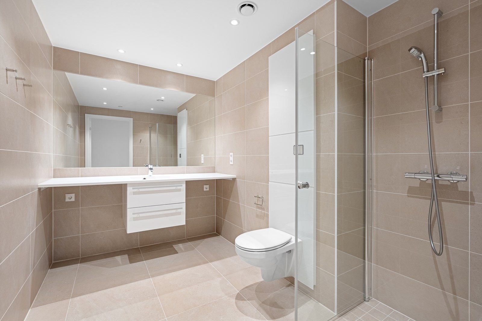 Badet er helfliset med varme i gulvet. Det er avsatt plass til vaskemaskin og tørketrommel under benkeplate i tilknytting til baderomsinnredningen. Ellers inneholder badet vegghengt toalett, samt dusjnisje med innfellbare dusjdører. Galleribilde