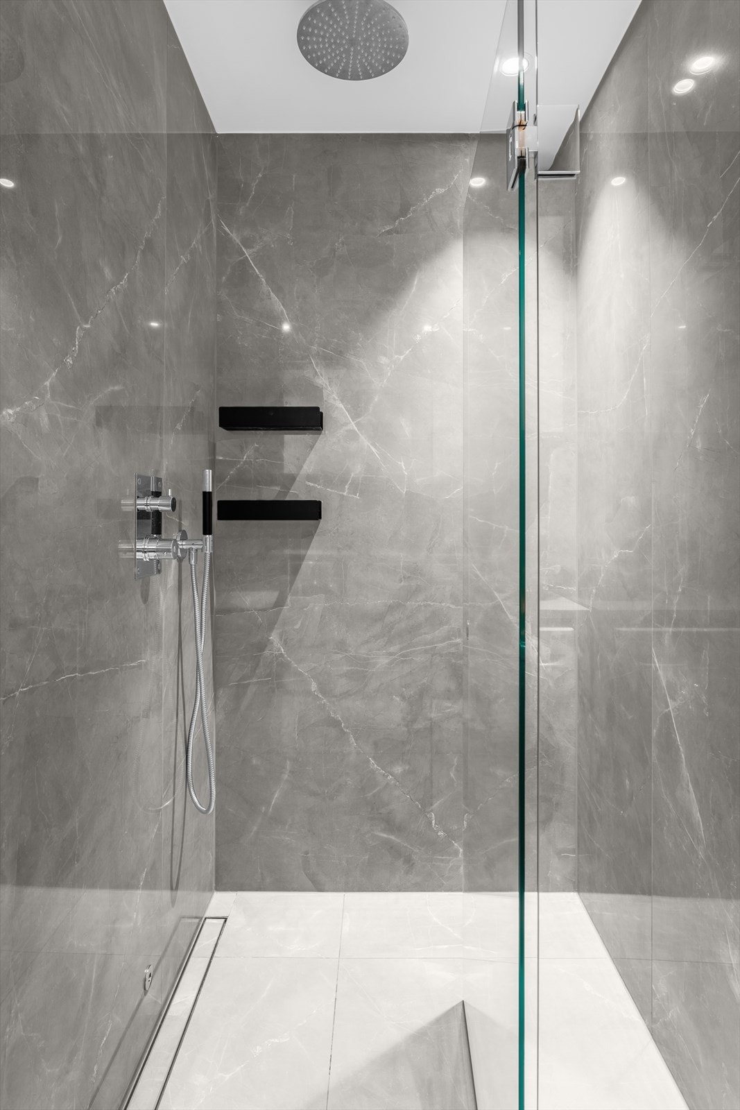 Stor dusjnisje med glassvegg/dør. Store fliser, hyller og tile-insert linjesluk. Fukt- og bryterstyrt avtrekksvifte i himling. Galleribilde