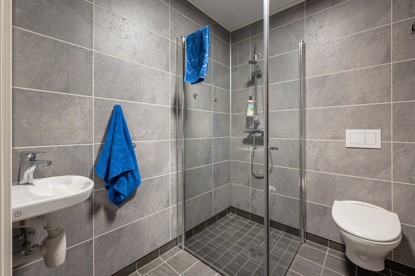 Badet er utstyrt med dusjhjørne med innfellbare dusjdører, vegghengt toalett og servant. Galleribilde