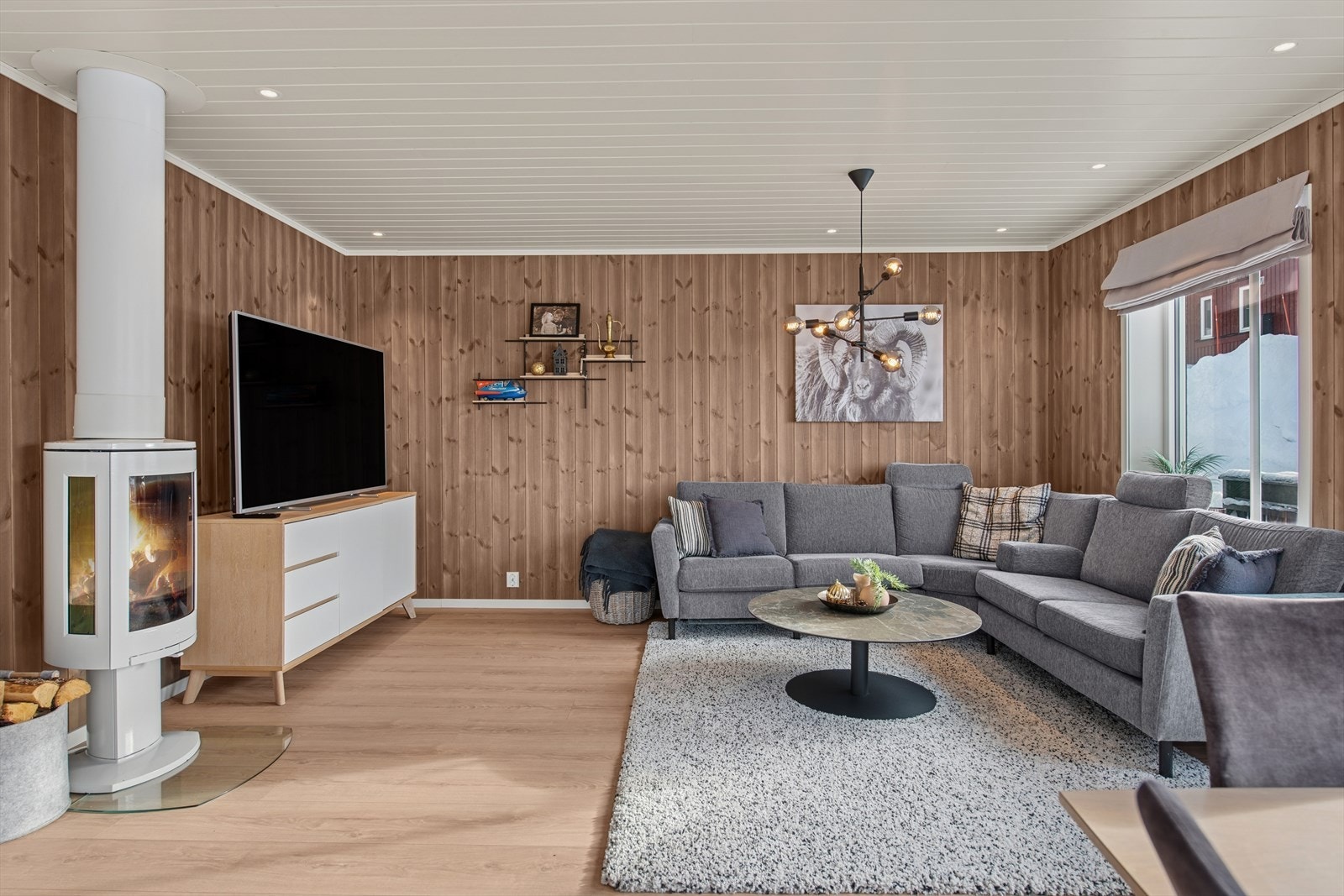 I den andre delen av stuen er sittegruppen plassert, med TV på benk og et elegant ildsted i hvit utførelse som bidrar til både varme og en hyggelig atmosfære i rommet Galleribilde