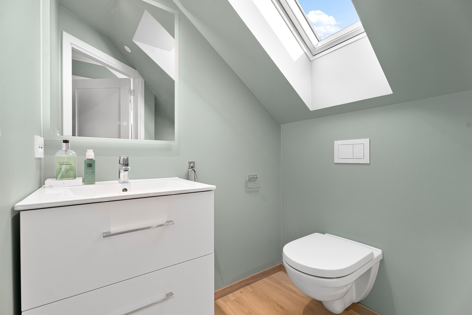 Toalettrom med vegghengt toalett, servant med oppbevaring samt speil. Galleribilde