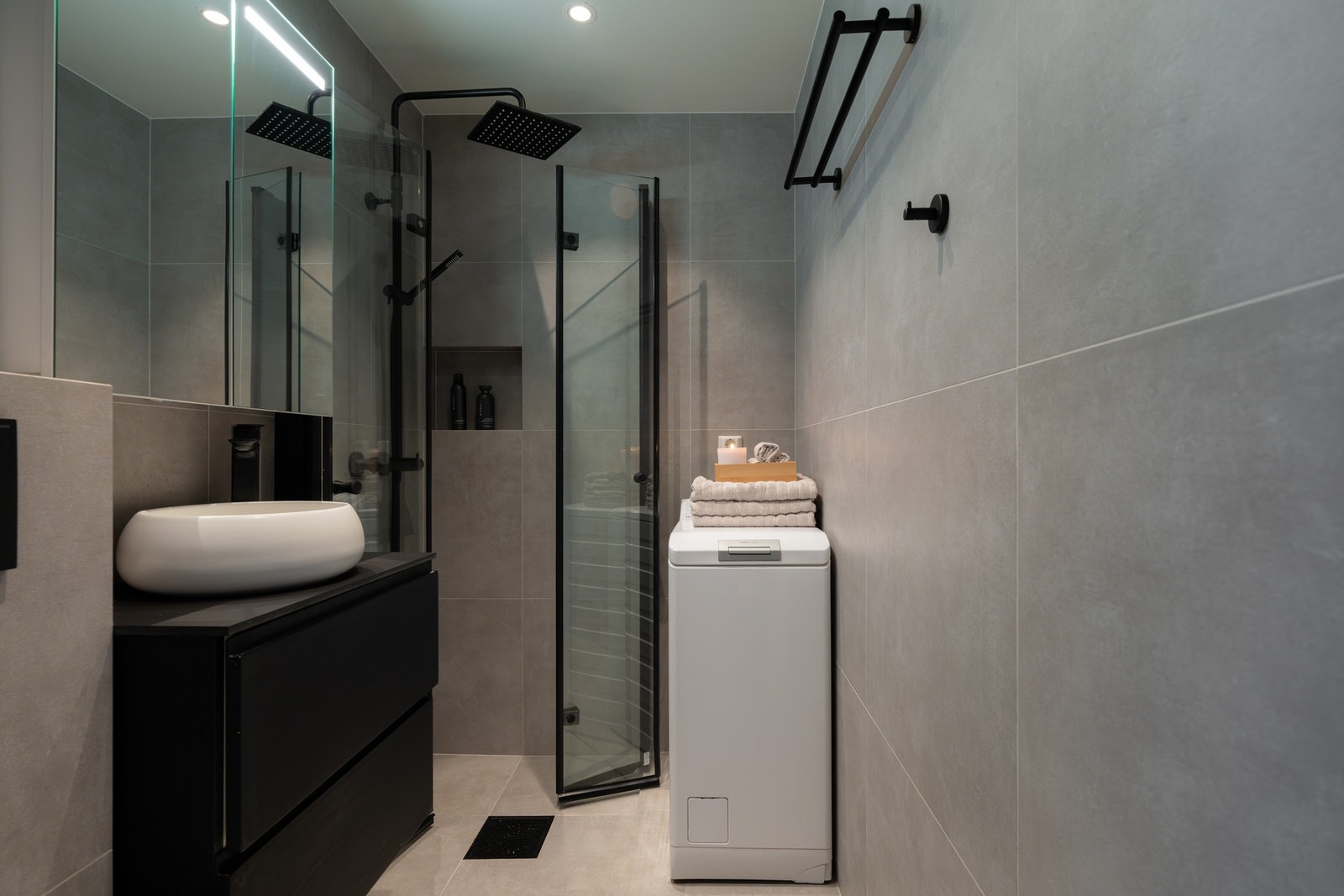 Badet er utstyrt med innredning med to skuffer med ovenpåliggende servant, samt speilskap med belysning. Videre er det vegghengt toalett, samt regnfalldusj med innfellbare dusjdører og en praktisk innfelt hylleløsning i dusjsonen. Galleribilde