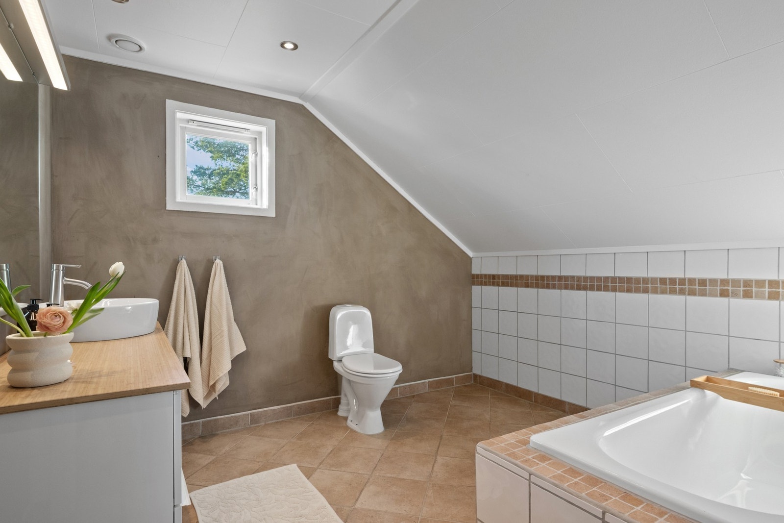 Badet har flislagt gulv i en jordtone, hvite veggfliser og vegger malt med kalkmaling. Galleribilde