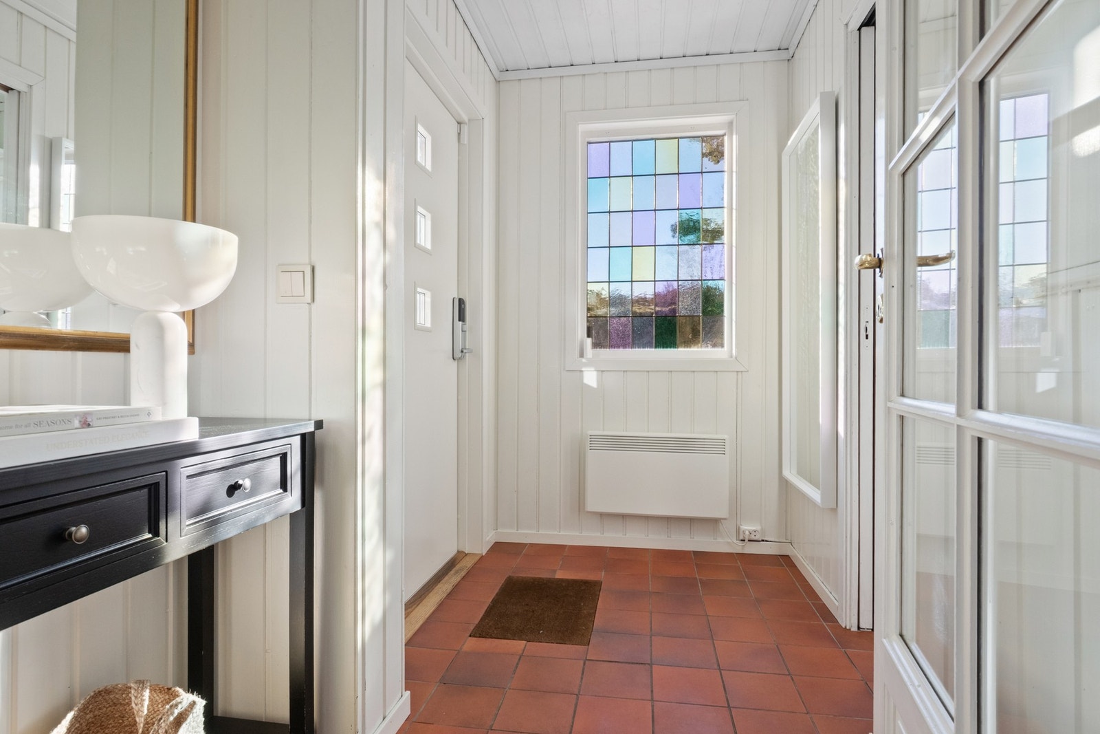 Entréen har et dekorativt blyglassvindu, hvitmalte panelvegger og terrakottafliser på gulvet. Galleribilde