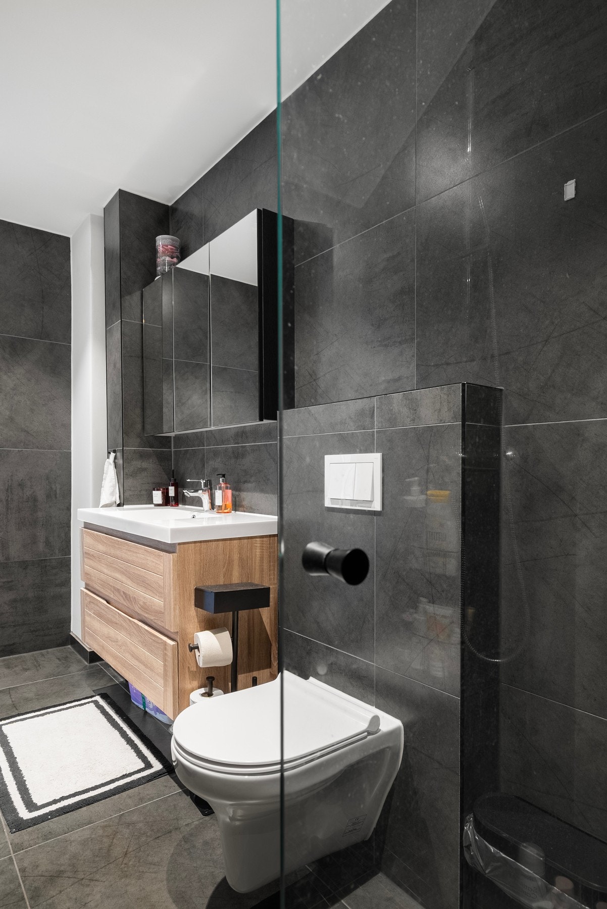 Et moderne bad med dusjhjørne, vegghengt toalett, opplegg til vaskemaskin, servantinnredning og speilskap Galleribilde