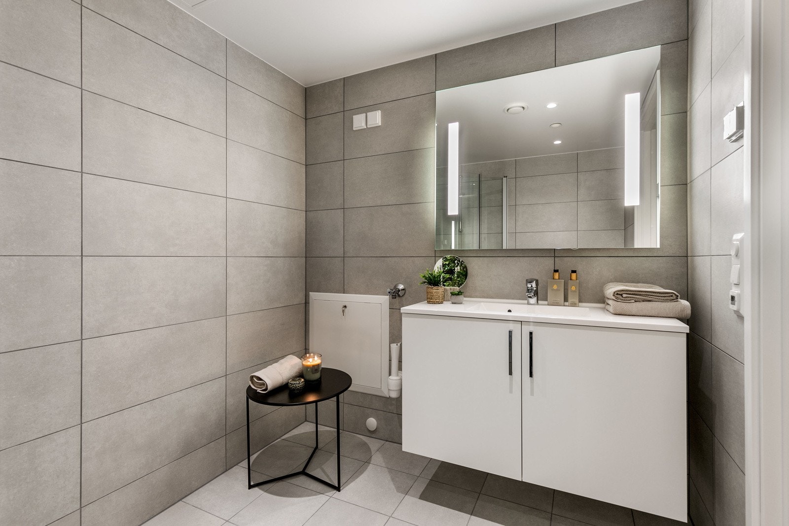 Badet har vegghengt toalett med innbygget sisterne, servant med skapinnredning samt speil med belysning. Galleribilde