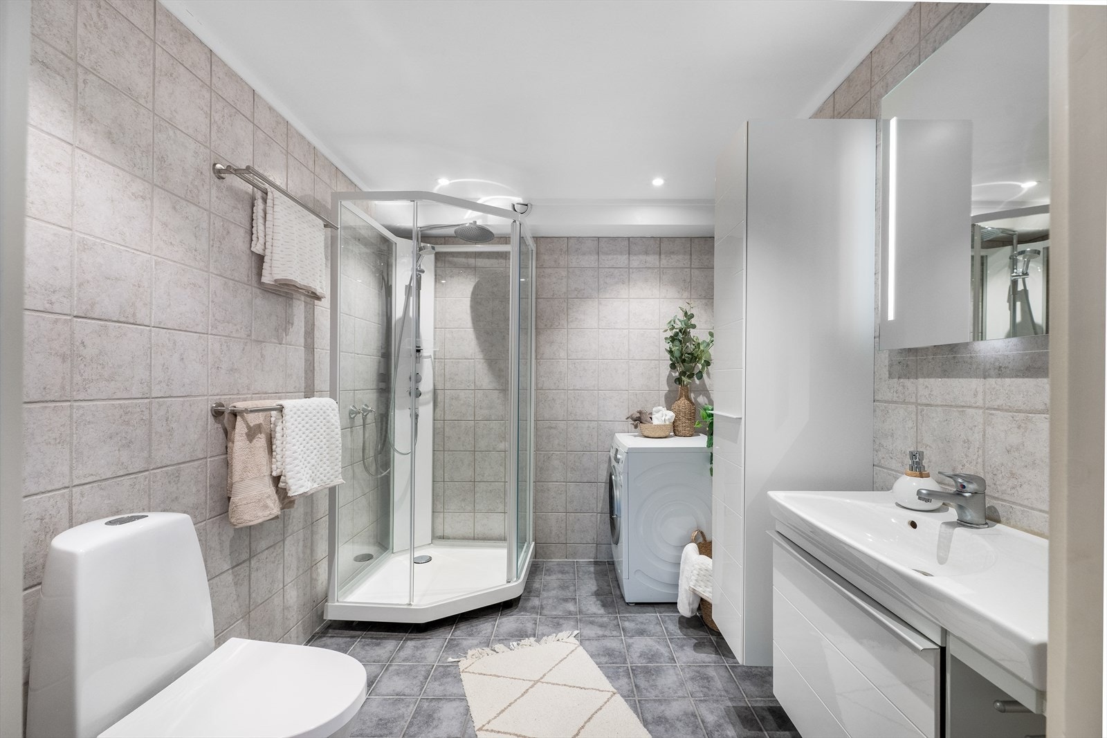 Pent flislagt bad med underliggende varme i gulv. Badet er videre innredet med heldekkende servant, servantskap, speil med belysning, dusjkabinett med regnfallsdusj, gulvstående toalett, høyskap og opplegg for vaskemaskin/tørketrommel. Galleribilde