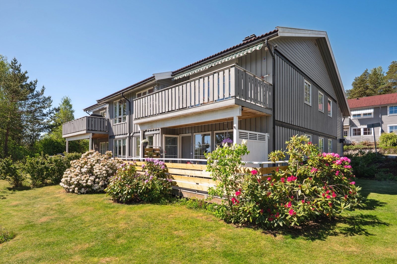 Sommerbilde - boligen har en pent opparbeidet hage med plenareal, prydbusker og hekk Galleribilde